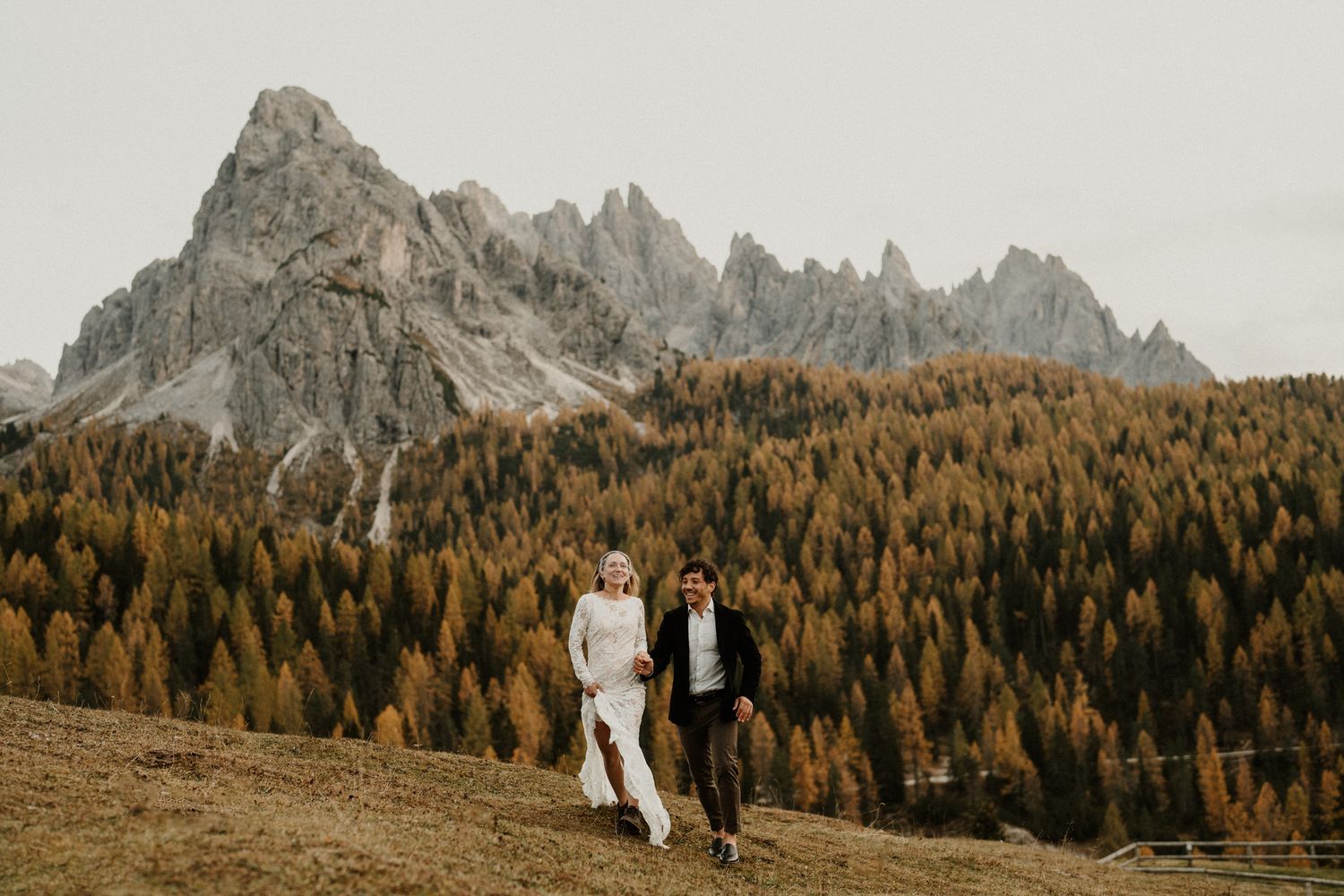 Couple walking through an alpine meadow with towering Dolomite peaks in the distance.