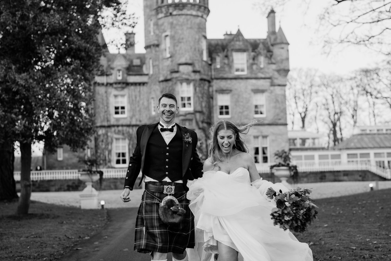 Black and white portrait of newlyweds in front of historic Scottish castle.