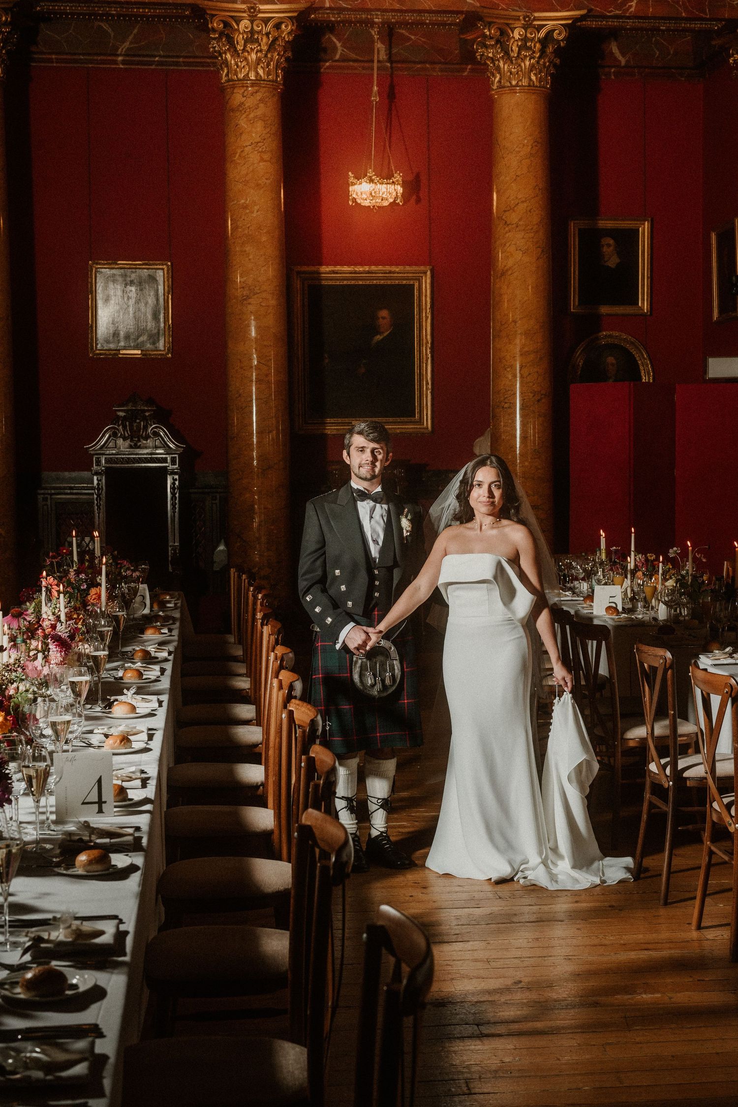 Wedding reception setup in elegant dining room with red walls and ornate columns.
