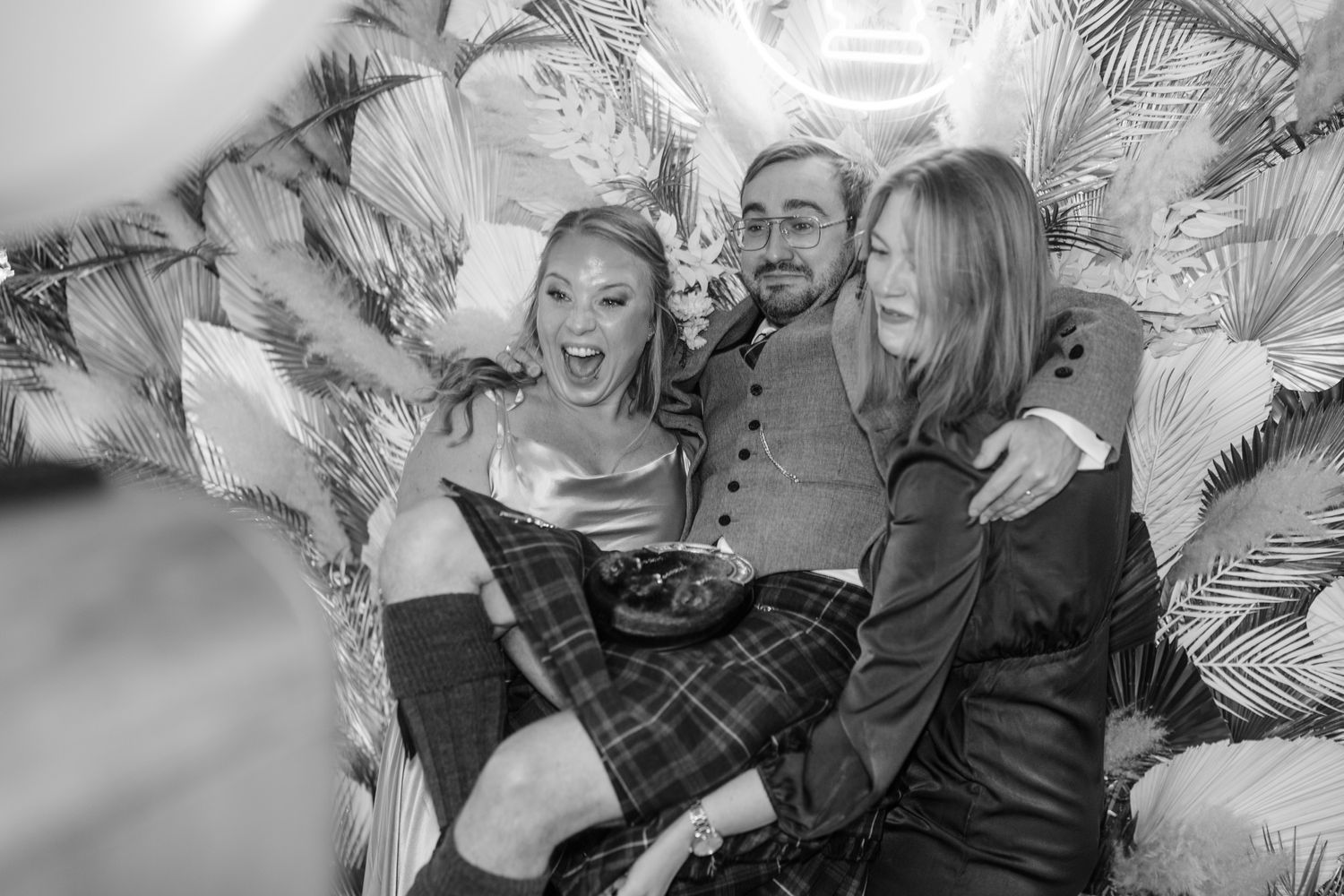 Black and white photo capturing joyful moment at wedding celebration with tropical backdrop.