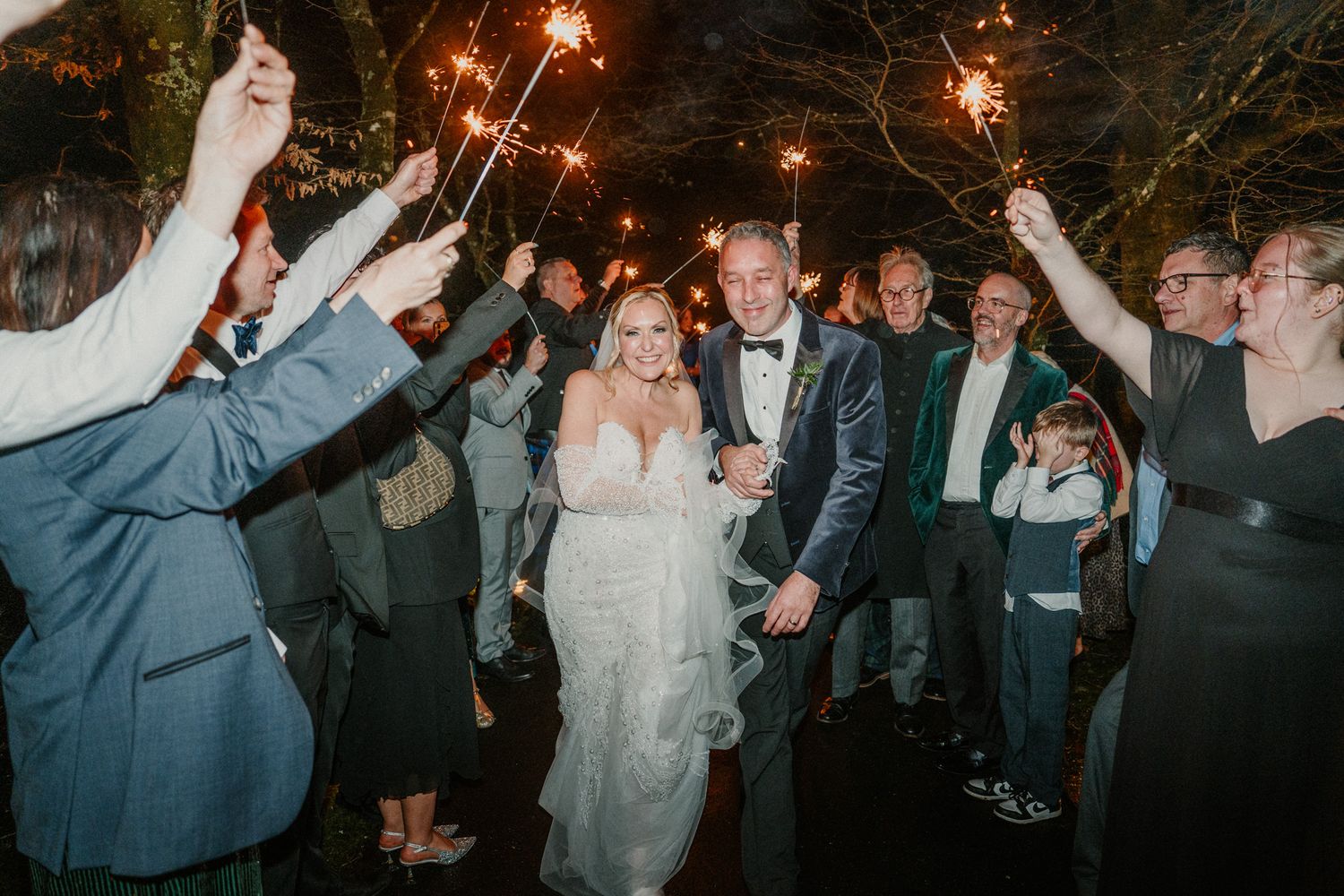 Wedding party celebrates with sparklers under the night sky during outdoor reception.
