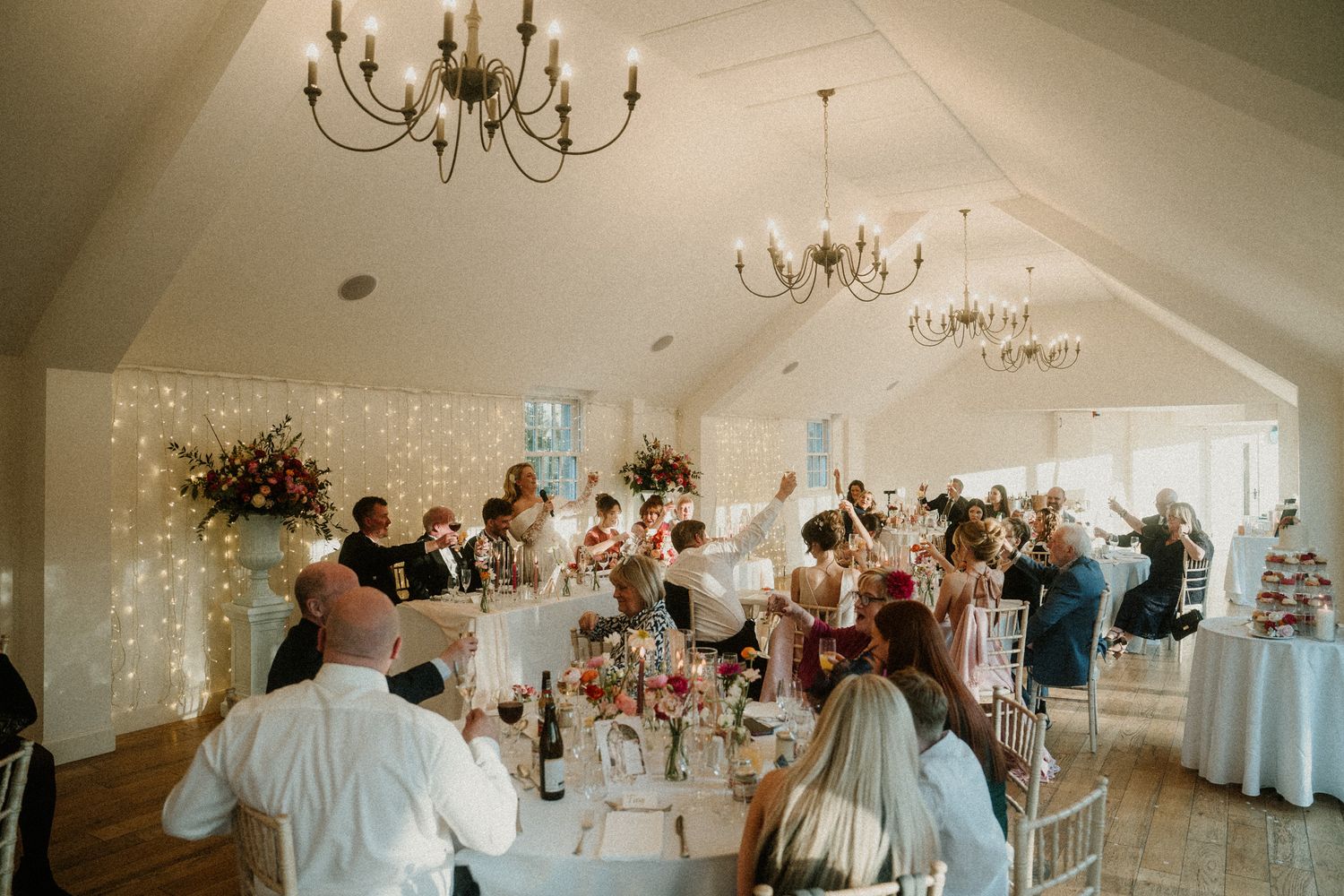 Panoramic view of an elegant wedding reception hall with chandeliers and white decor.