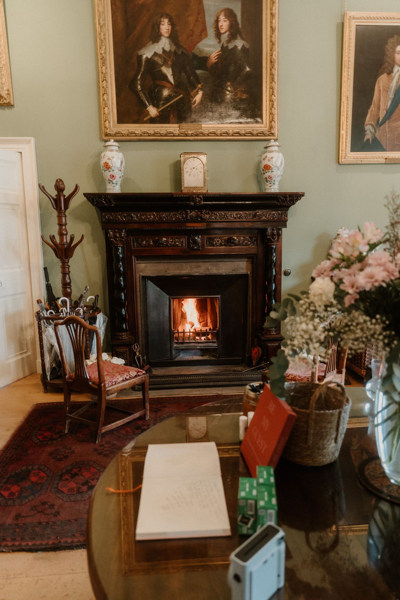 Elegant room with ornate fireplace, portrait paintings, floral arrangement, and antique furniture on a Persian rug.