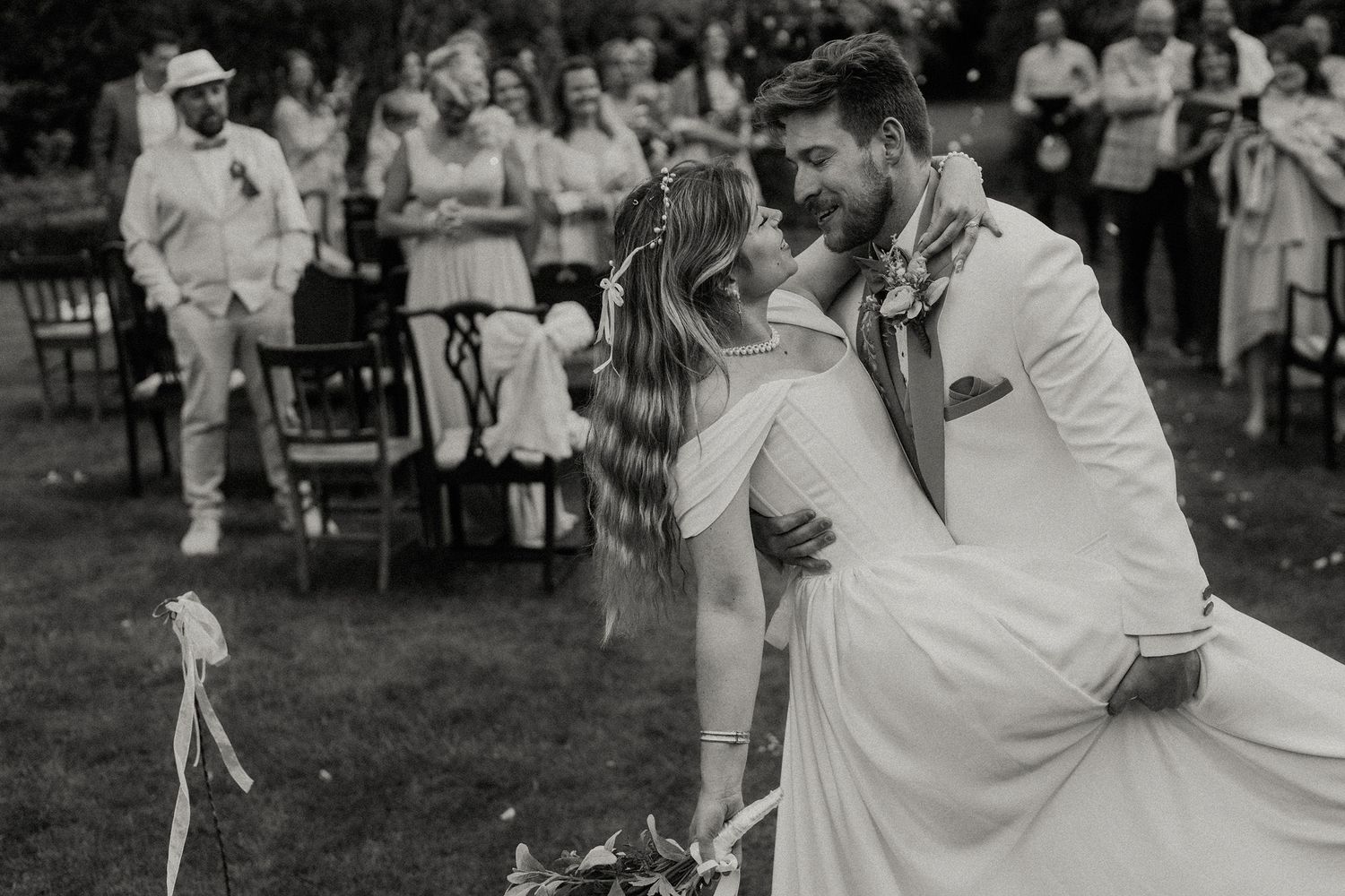 Black and white photo of a bride and groom sharing their first kiss at an outdoor wedding ceremony.
