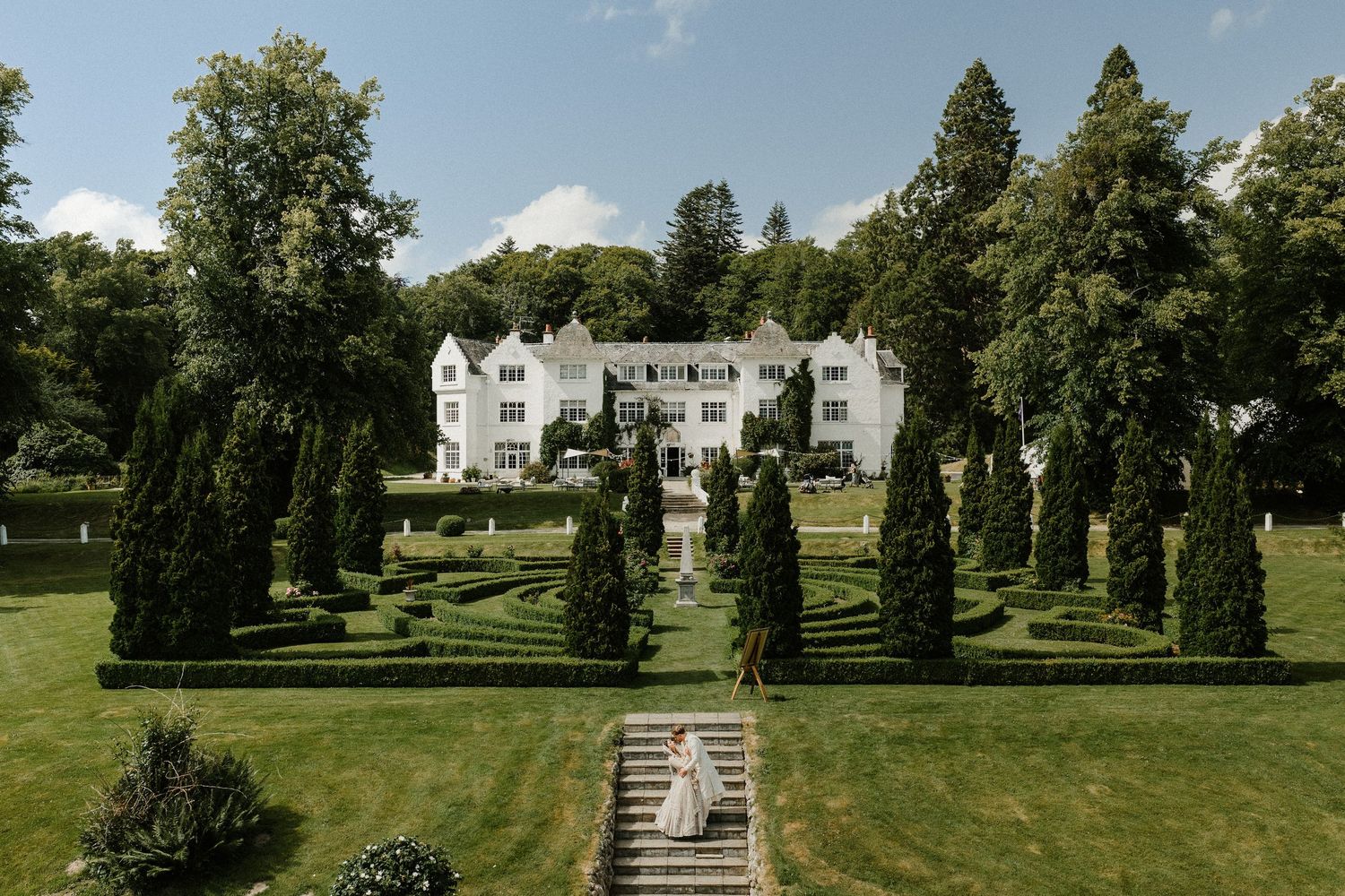 A series of scenic garden pathways with stone steps leading to a white mansion surrounded by manicured lawns and trees.