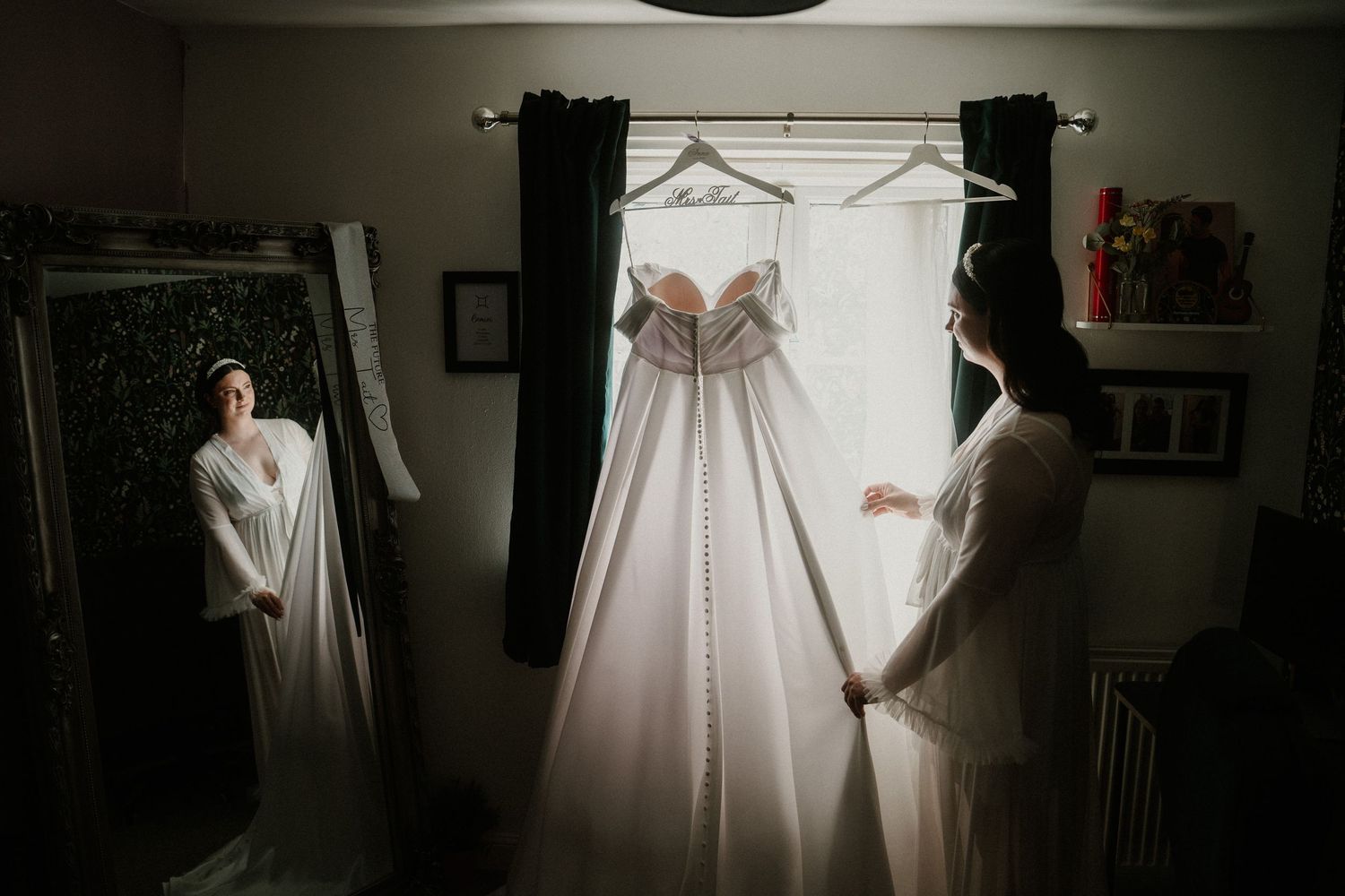 Wedding dress preparations in moody lighting with dramatic shadows and window light.