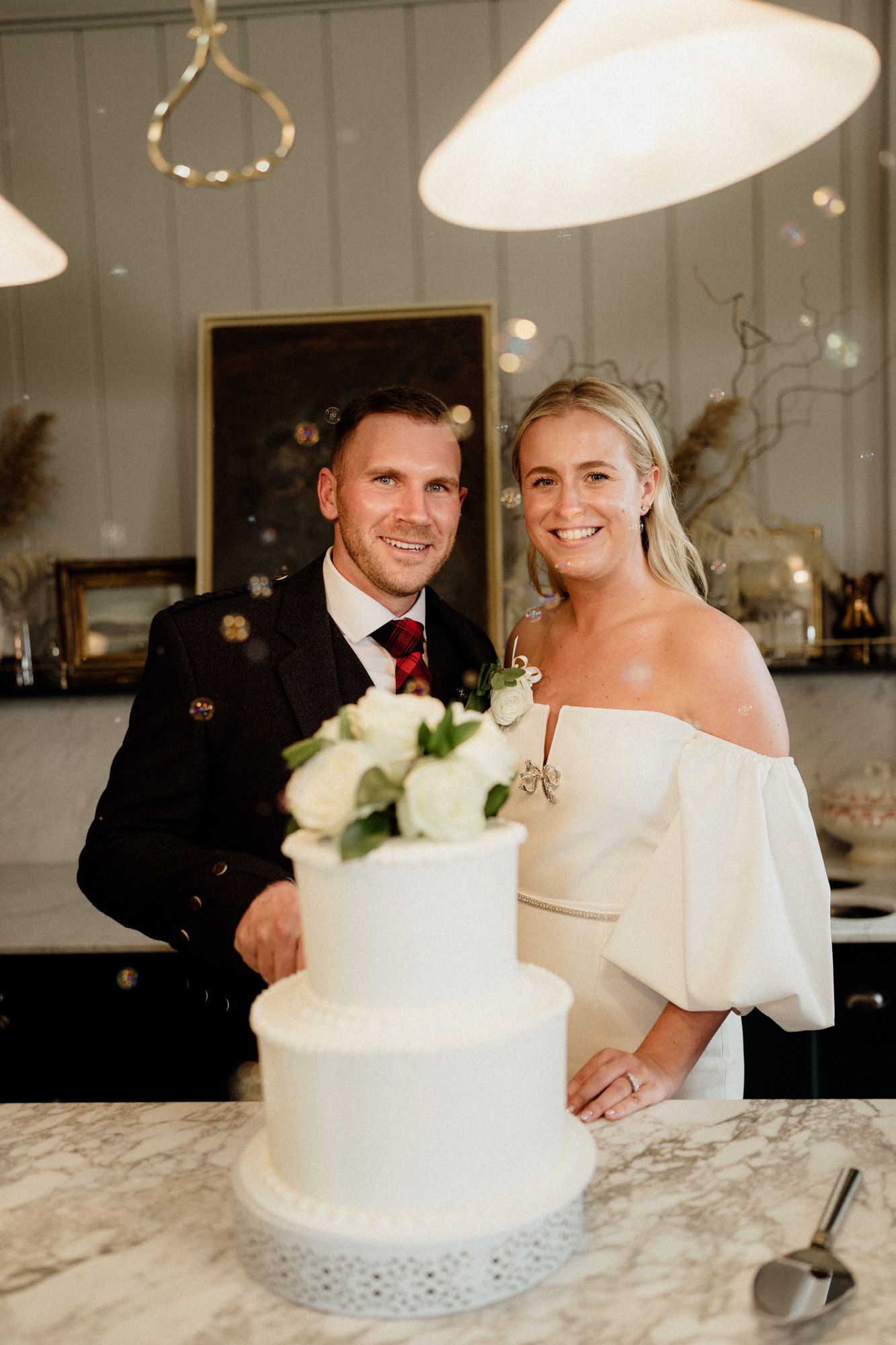 White wedding cake display on marble counter with delicate lace details and floral accents.