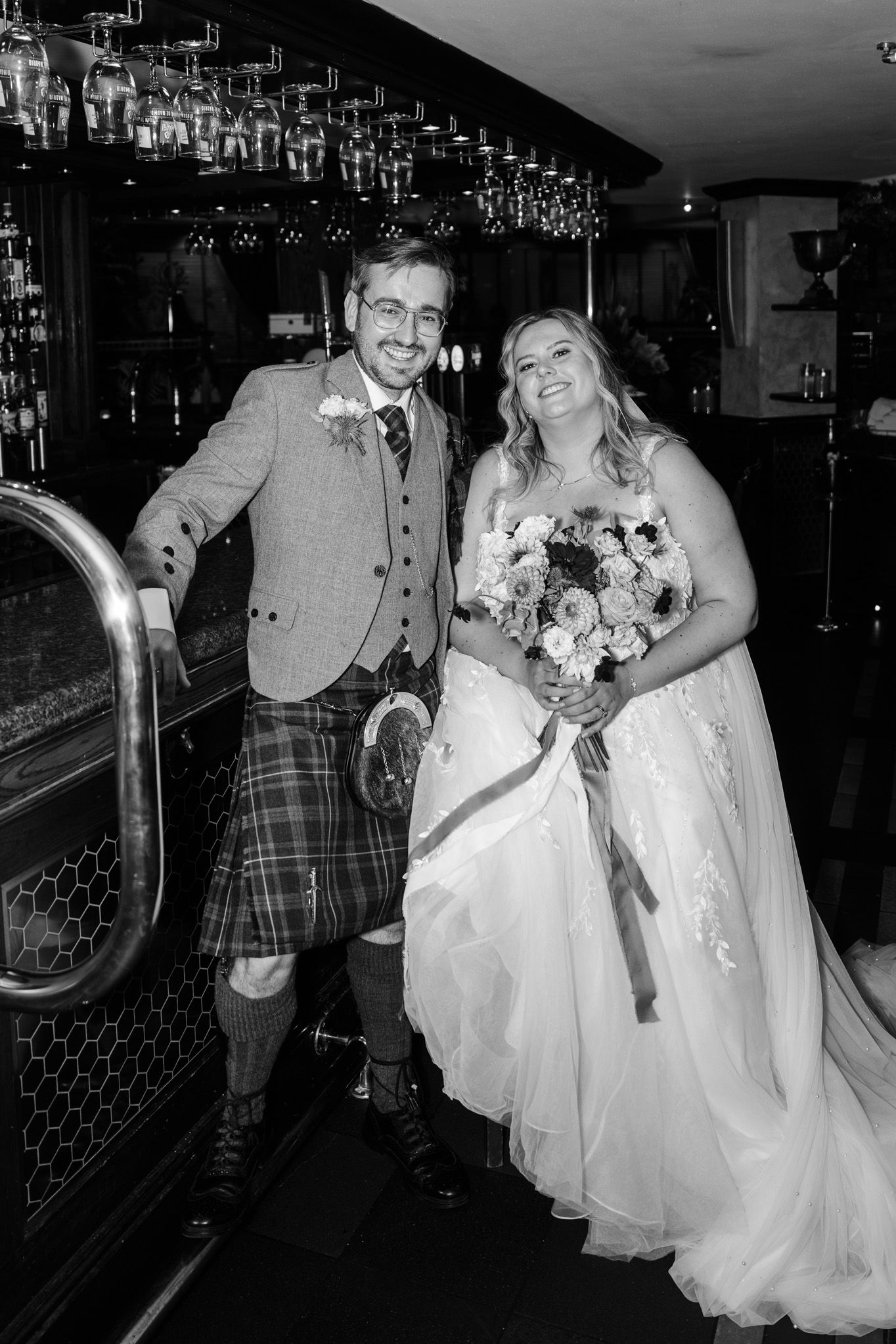 A wedding couple shares joyful moments together in a dark pub setting with a vintage bar backdrop.