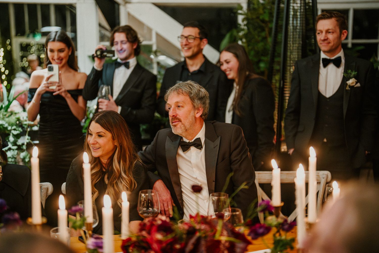 Candlelit reception table decorated with red floral arrangements and taper candles for an evening celebration.