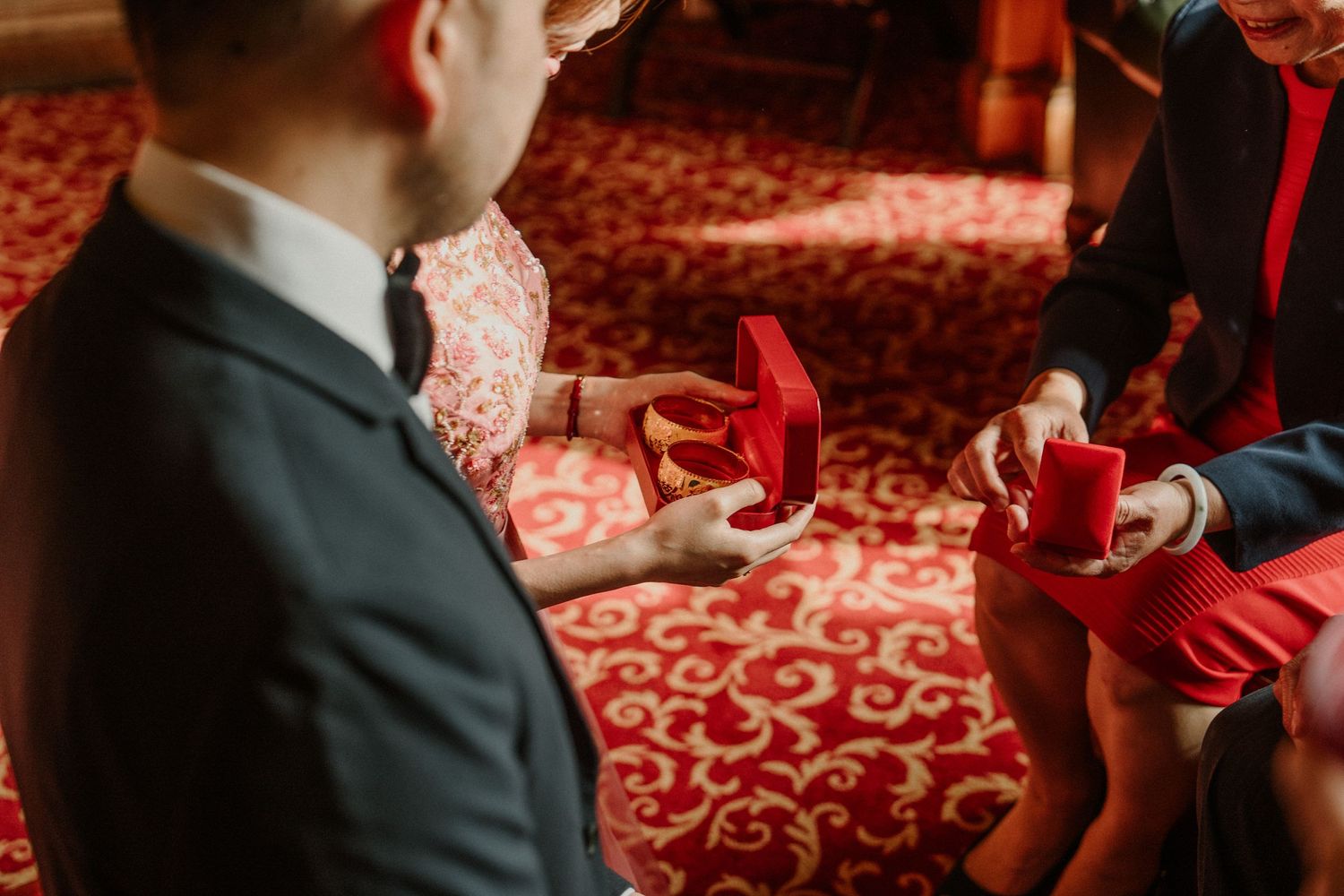 Close-up of formal attire and red accessories on ornate patterned carpet.