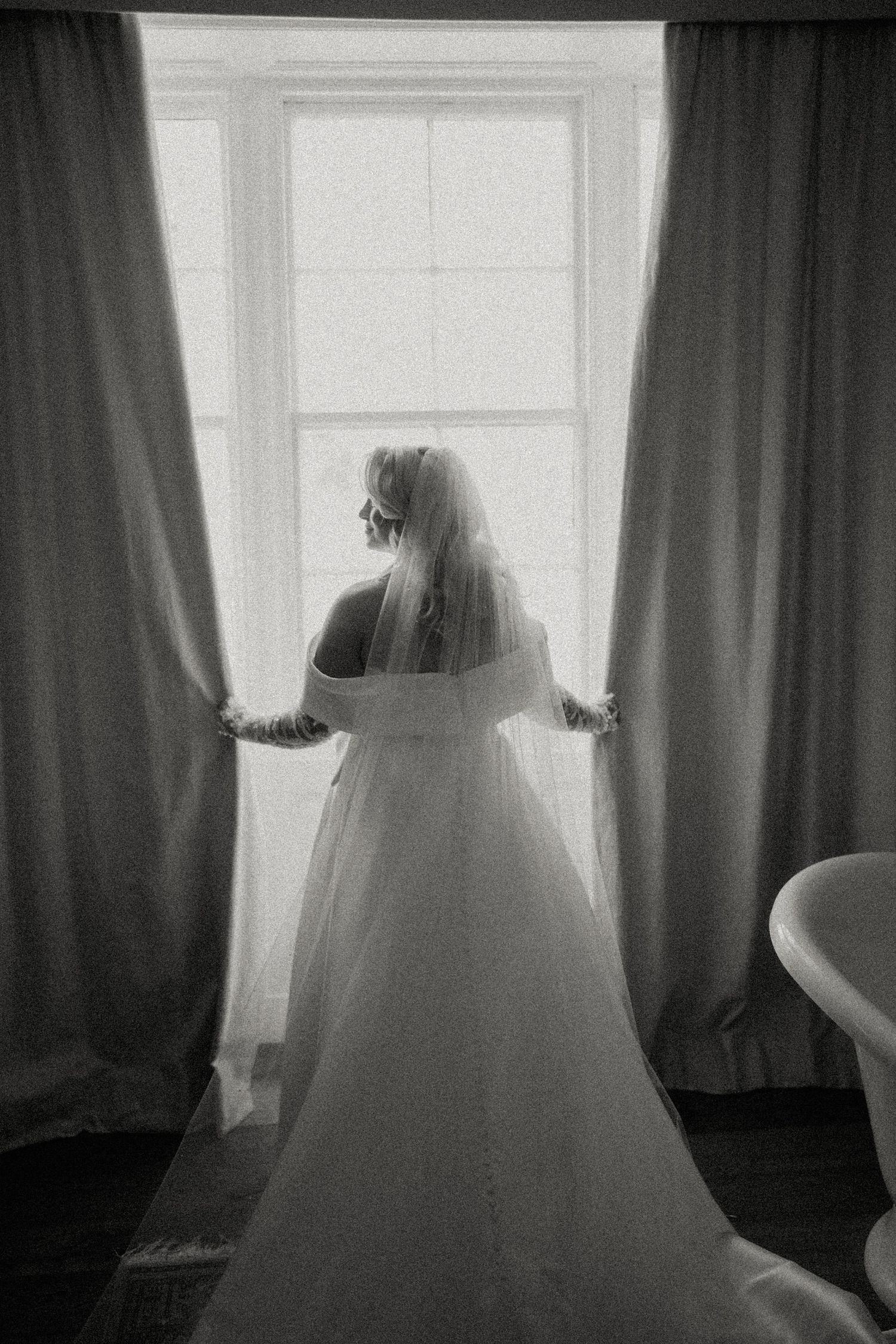 Silhouettes of a bride in a voluminous wedding dress against bright windows.