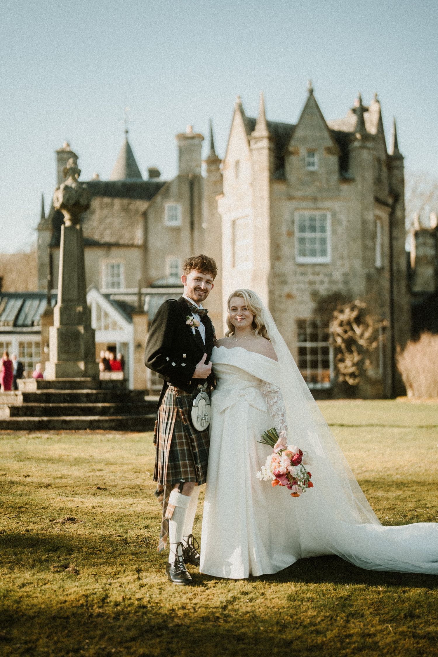 Scottish wedding portrait with castle backdrop featuring traditional highland dress and flowing white gown.