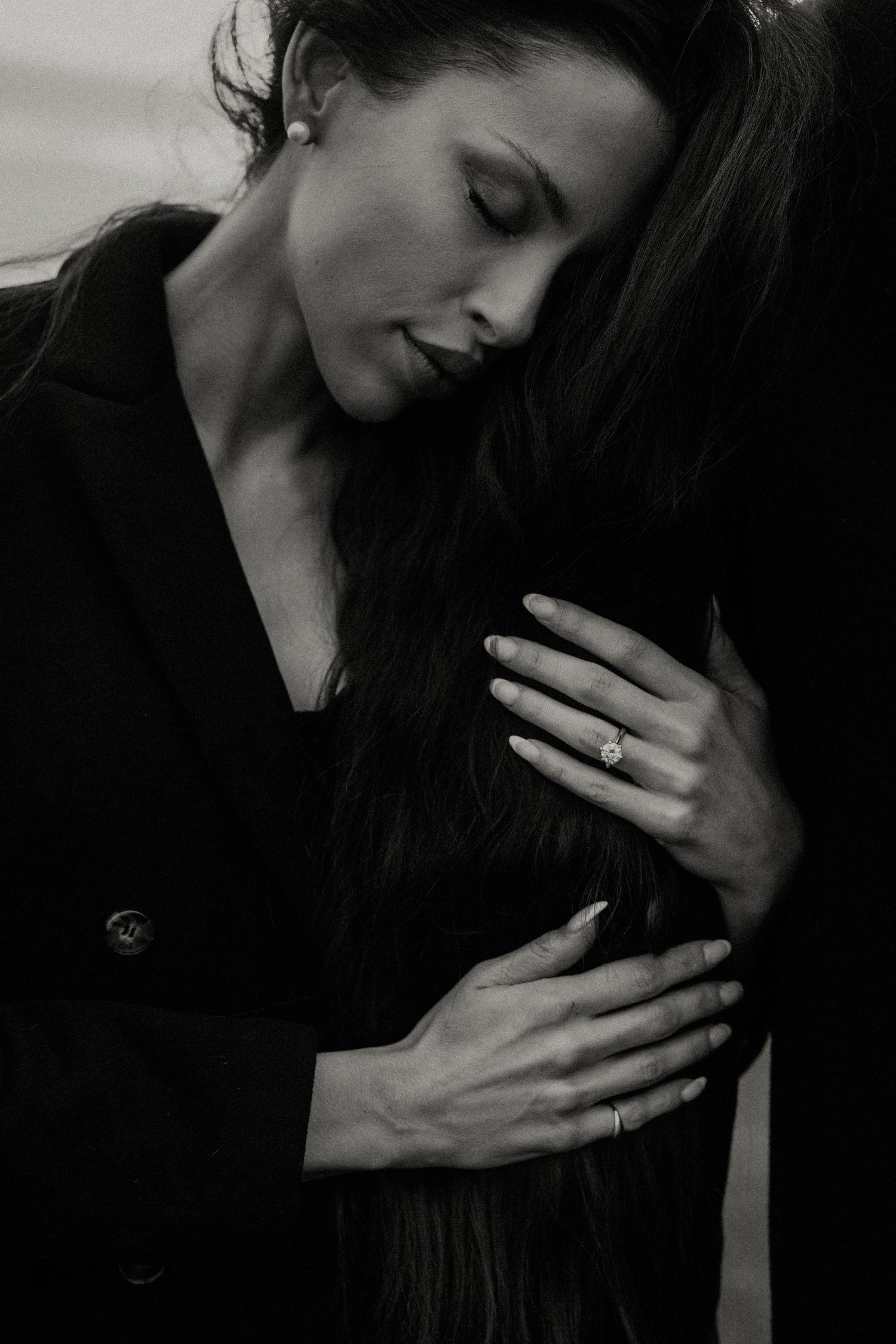 Dramatic black and white portrait of a woman in dark clothing with long hair and a contemplative expression.