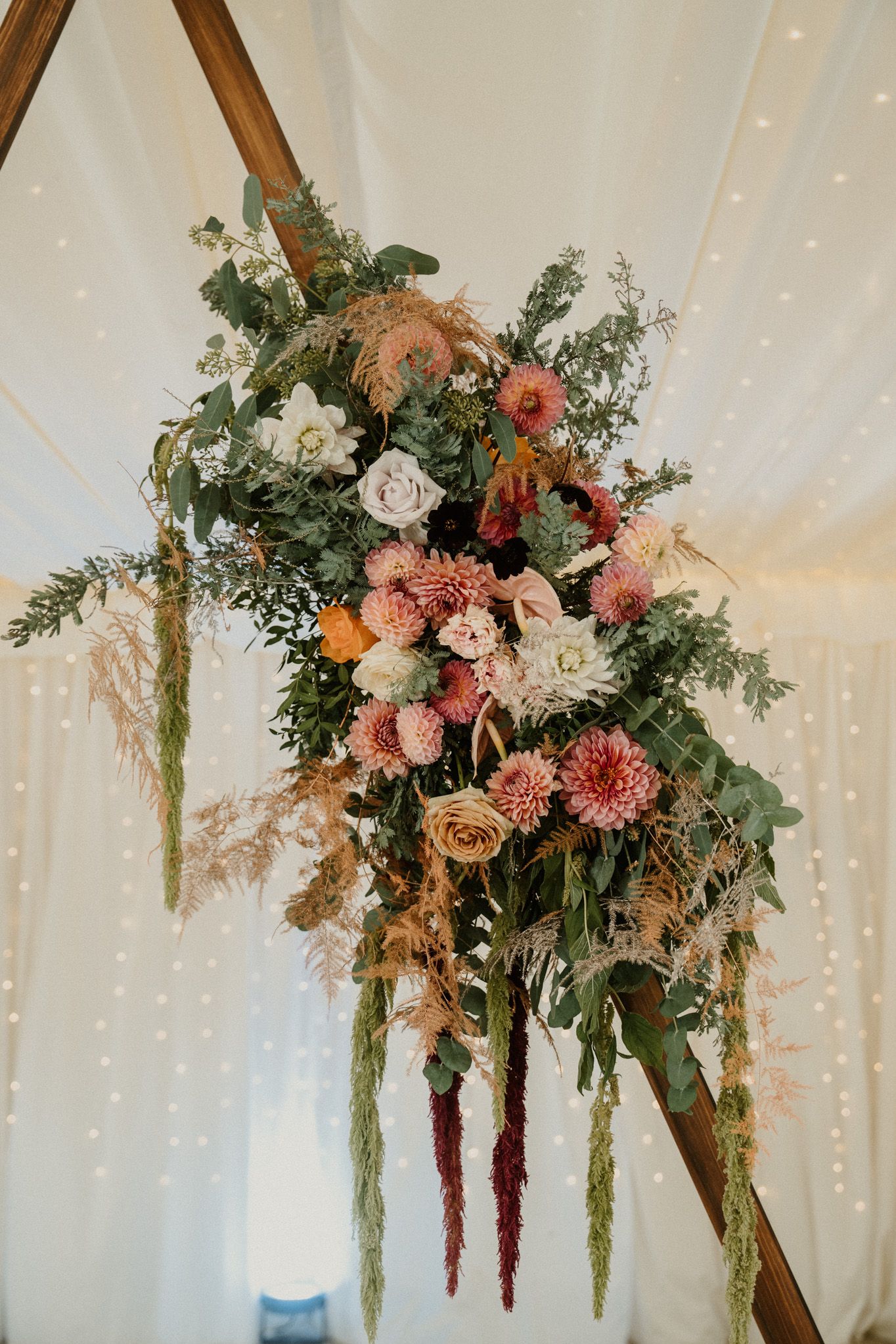 Stunning floral arrangement with pink blooms and greenery hanging from wooden triangle frame.