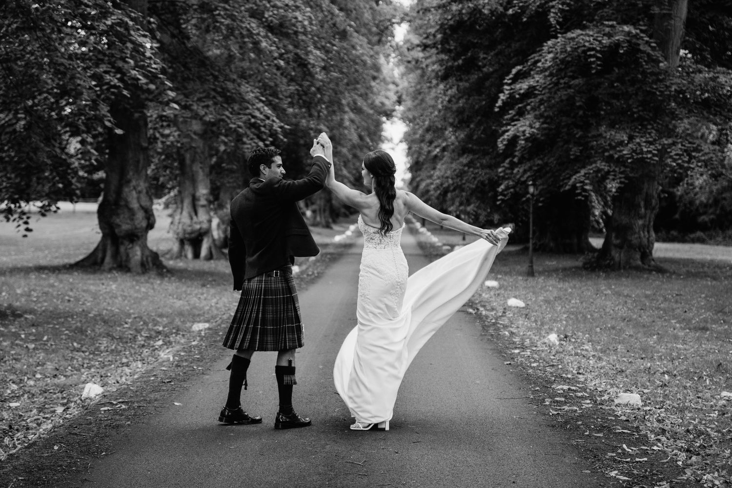 Black and white wedding photography on a scenic tree-lined pathway.