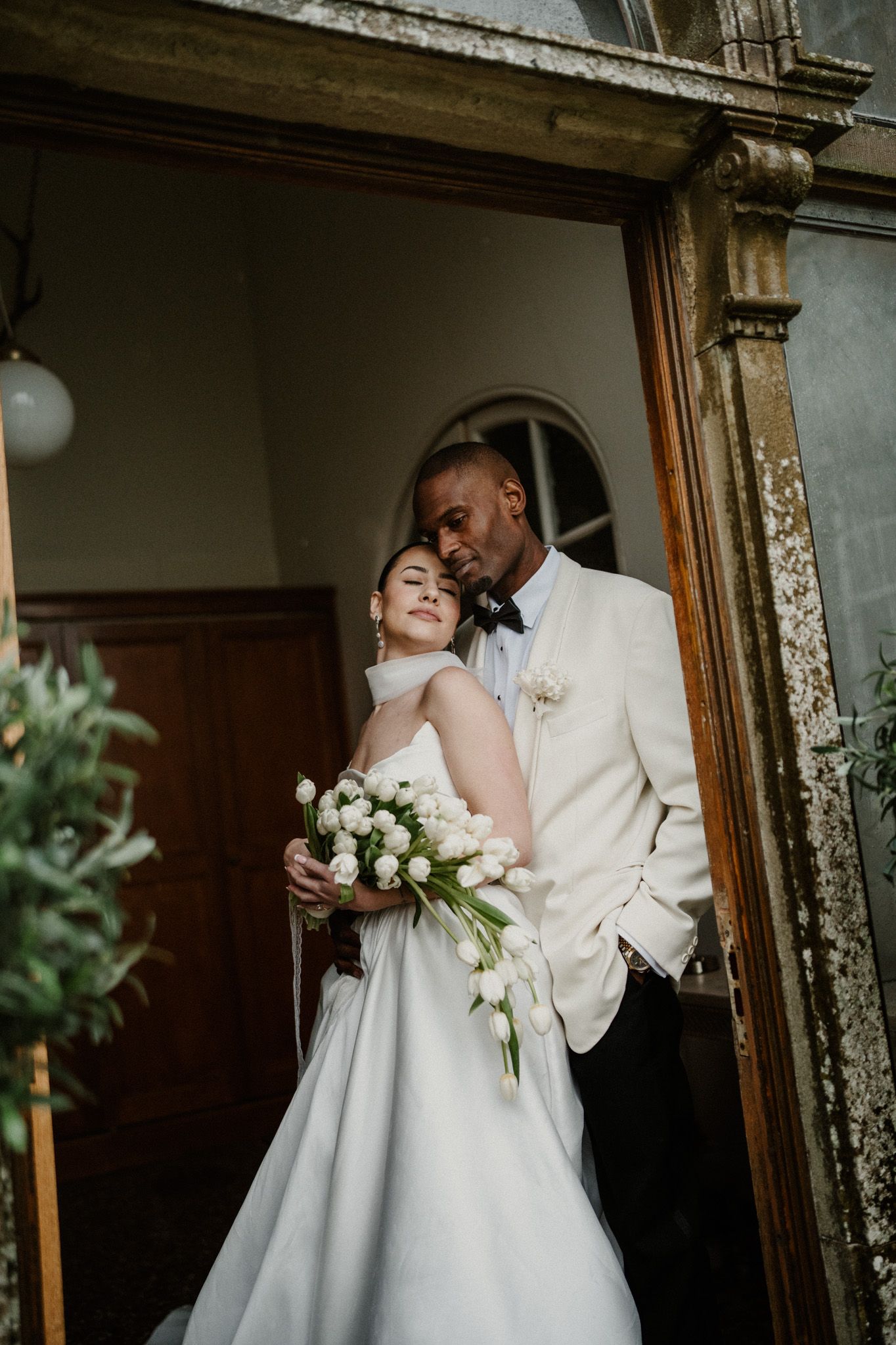 A romantic wedding couple embraces in front of ornate wooden doors in an elegant vintage setting.