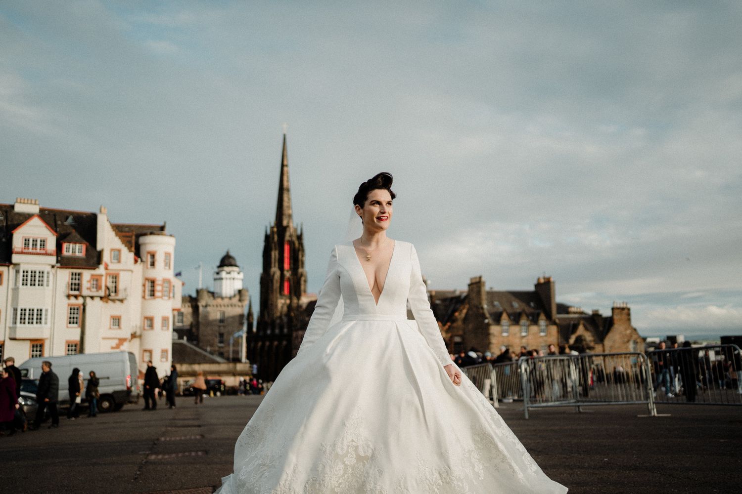 Wedding couple poses on Edinburgh castle grounds with city skyline in background.
