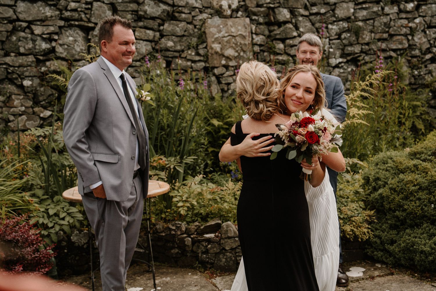 Emotional wedding moment in garden setting with stone wall backdrop.