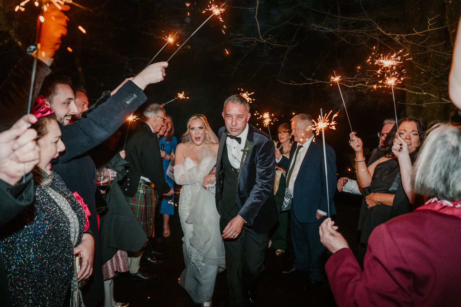 Wedding guests hold sparklers creating a magical nighttime celebration scene.