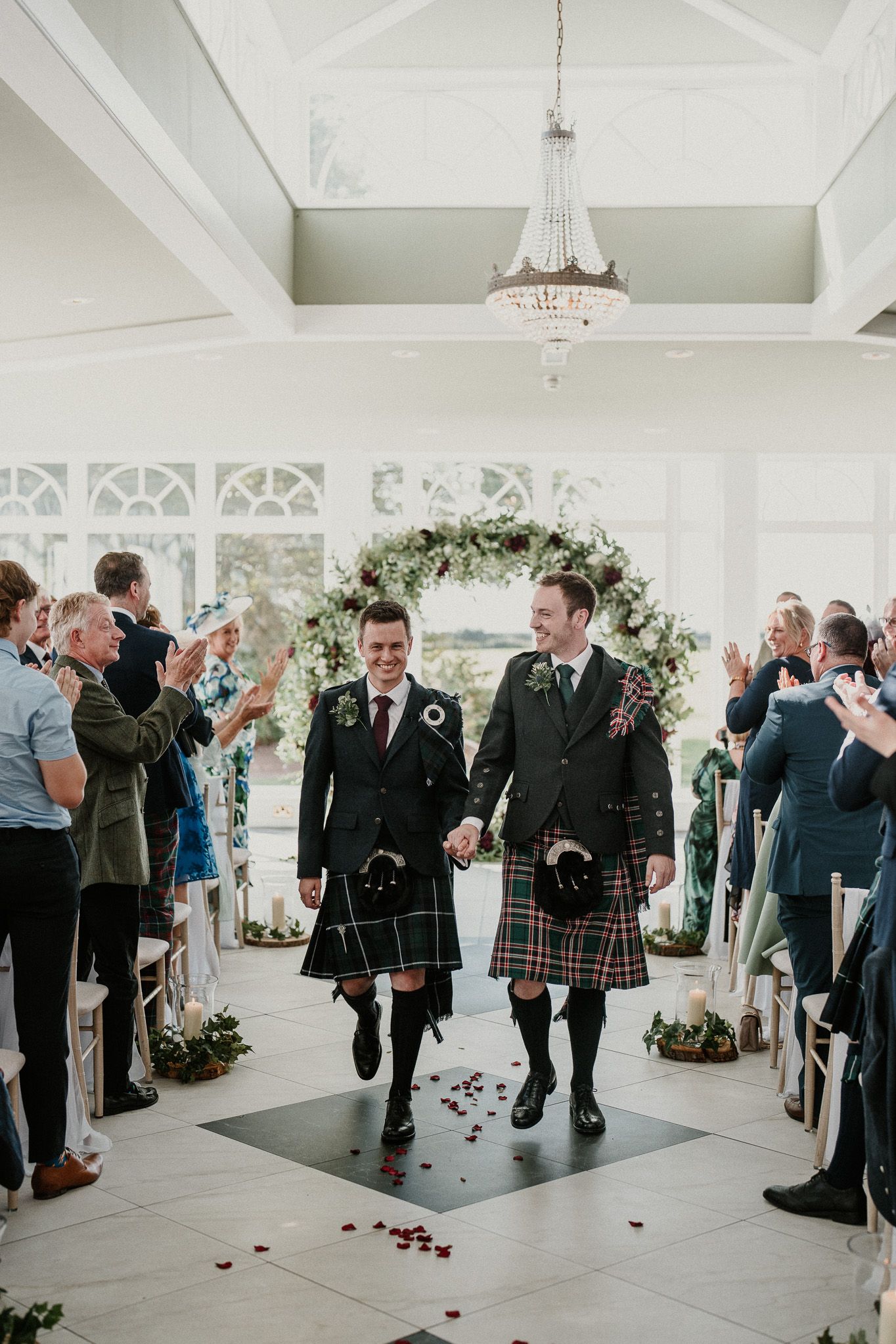 A couple in matching kilts walks down the aisle after their wedding ceremony.