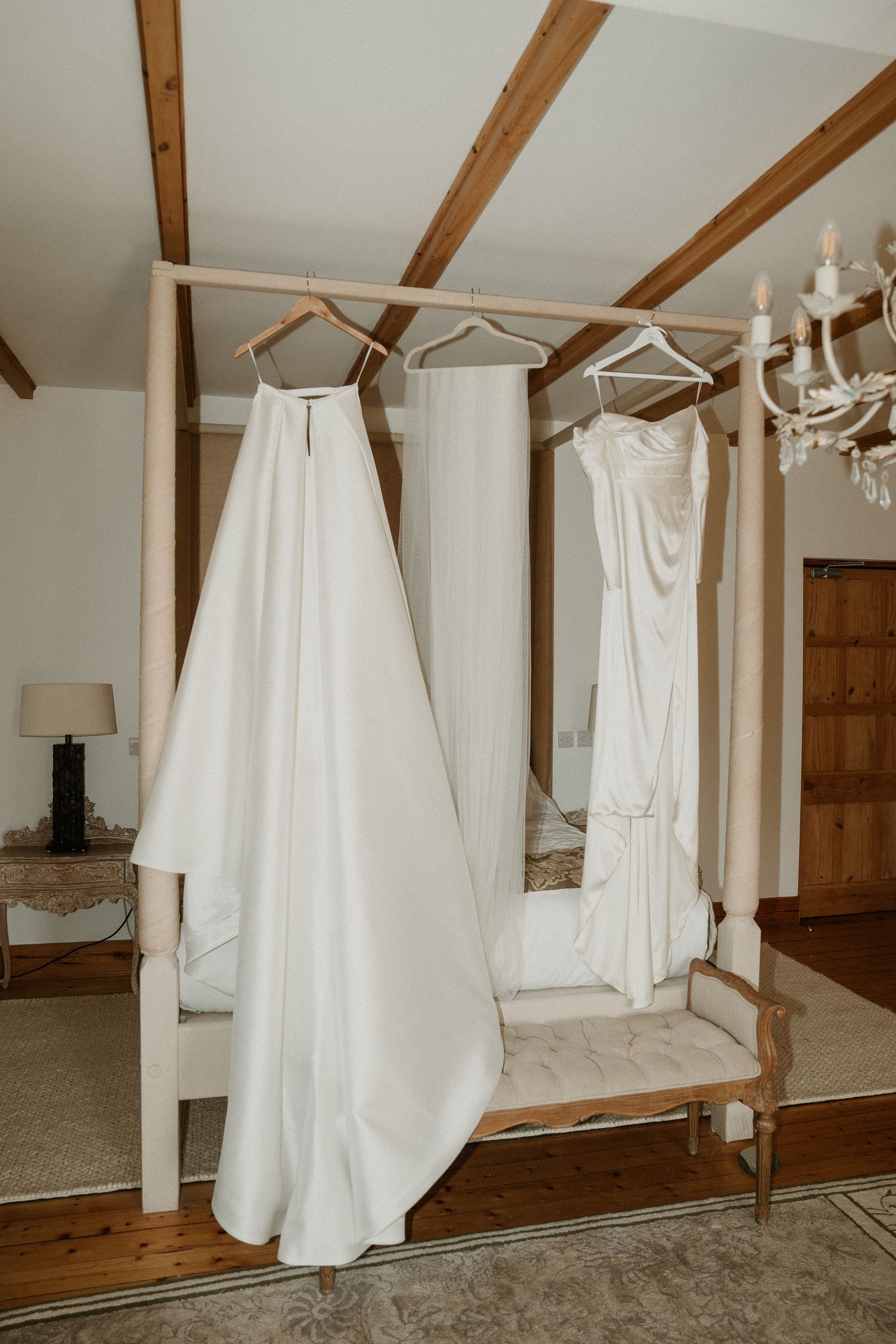 White wedding dresses hanging on display in a rustic room with wooden beams and chandelier.