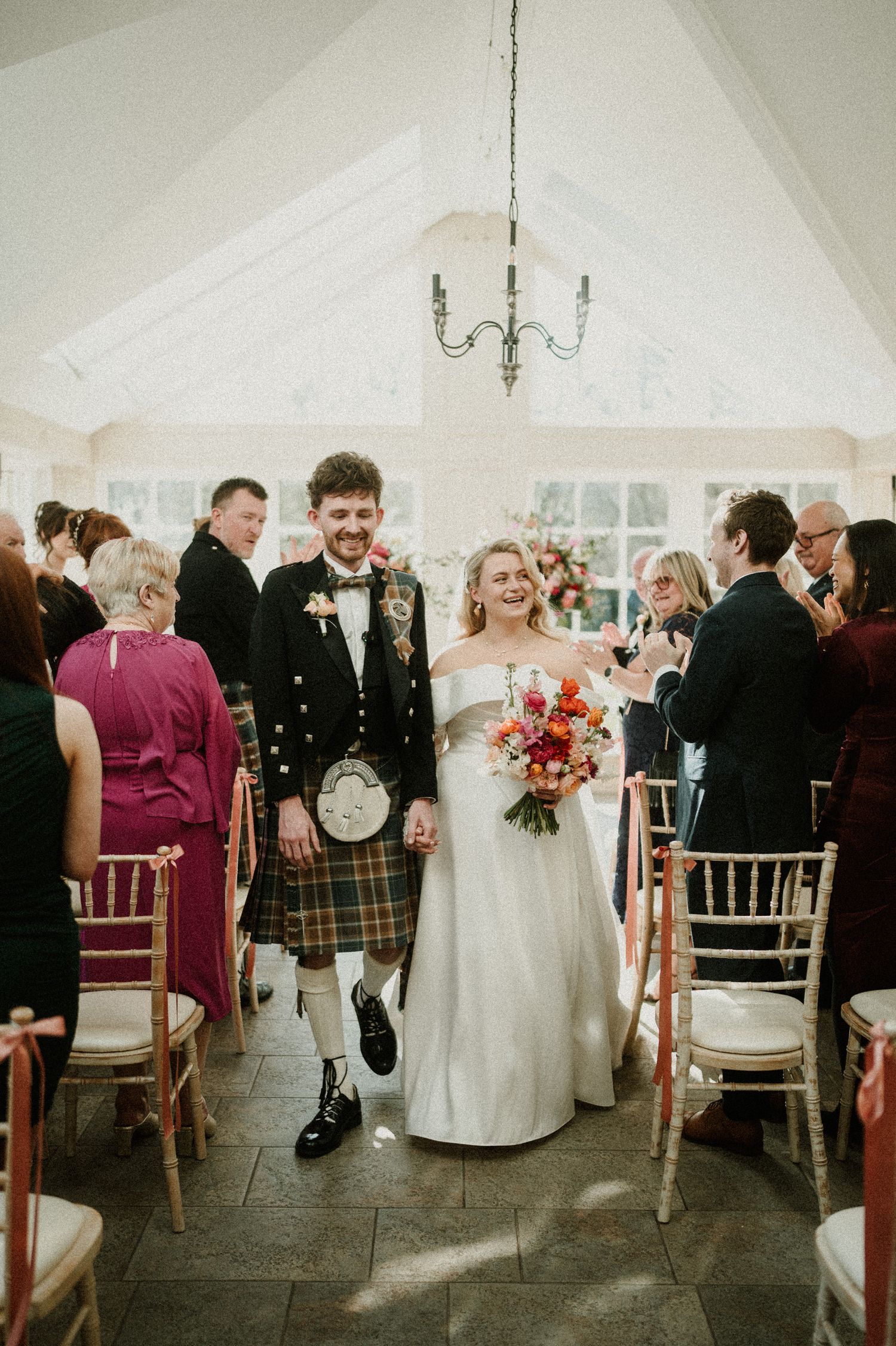 Happy couple walks down aisle after Scottish wedding ceremony in bright conservatory space.