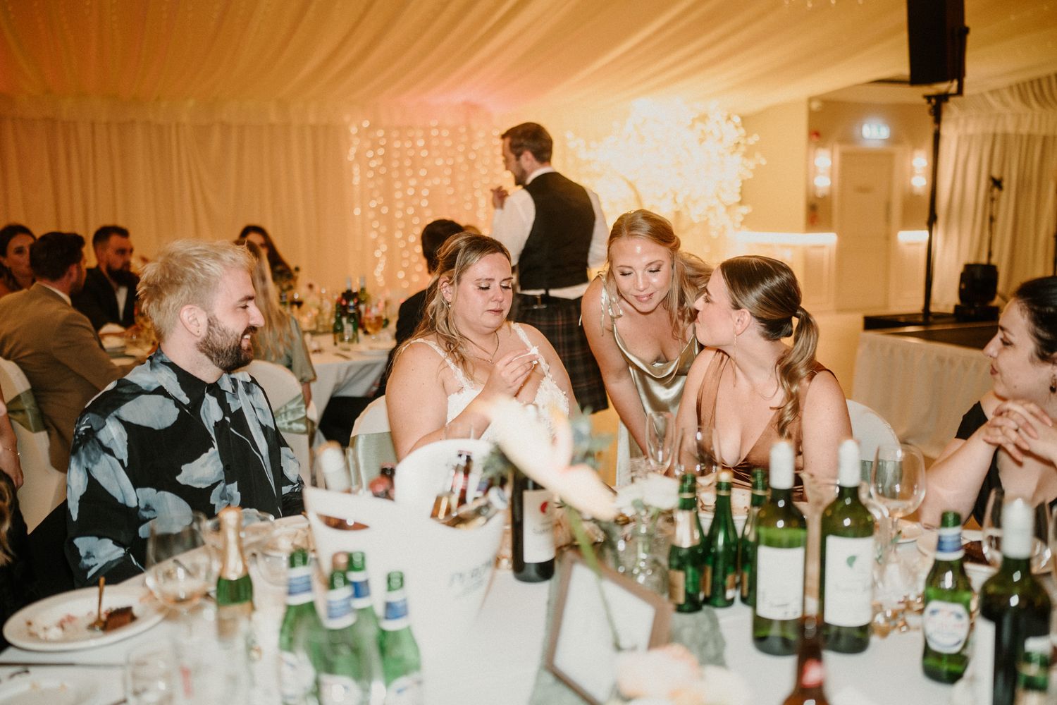 Candid moment of laughter shared at wedding reception table with drinks and decor.