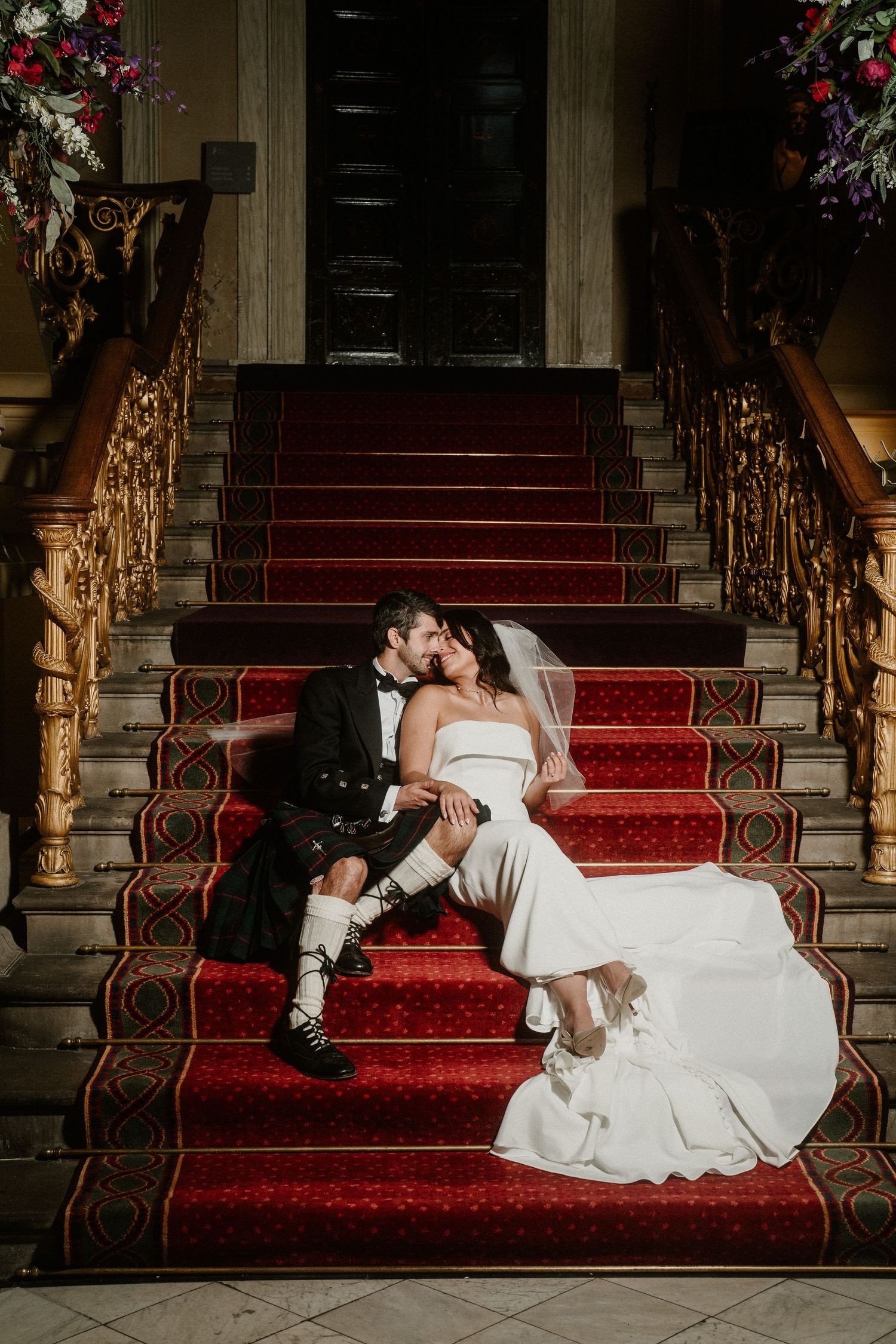 Romantic wedding photos on grand staircase with red carpet runner.