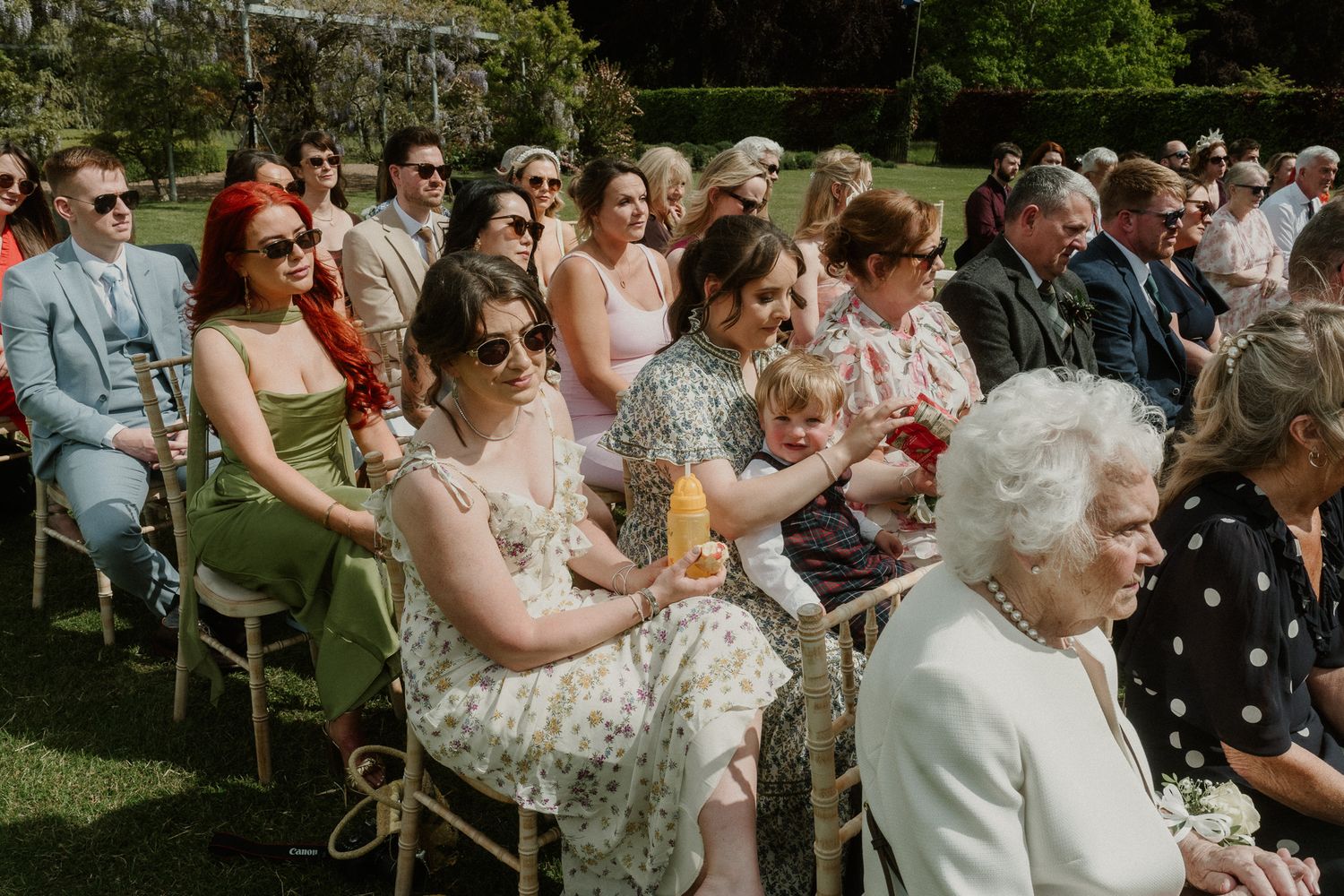 Guests seated outdoors at a wedding ceremony, enjoying a sunny day in colorful summer attire.