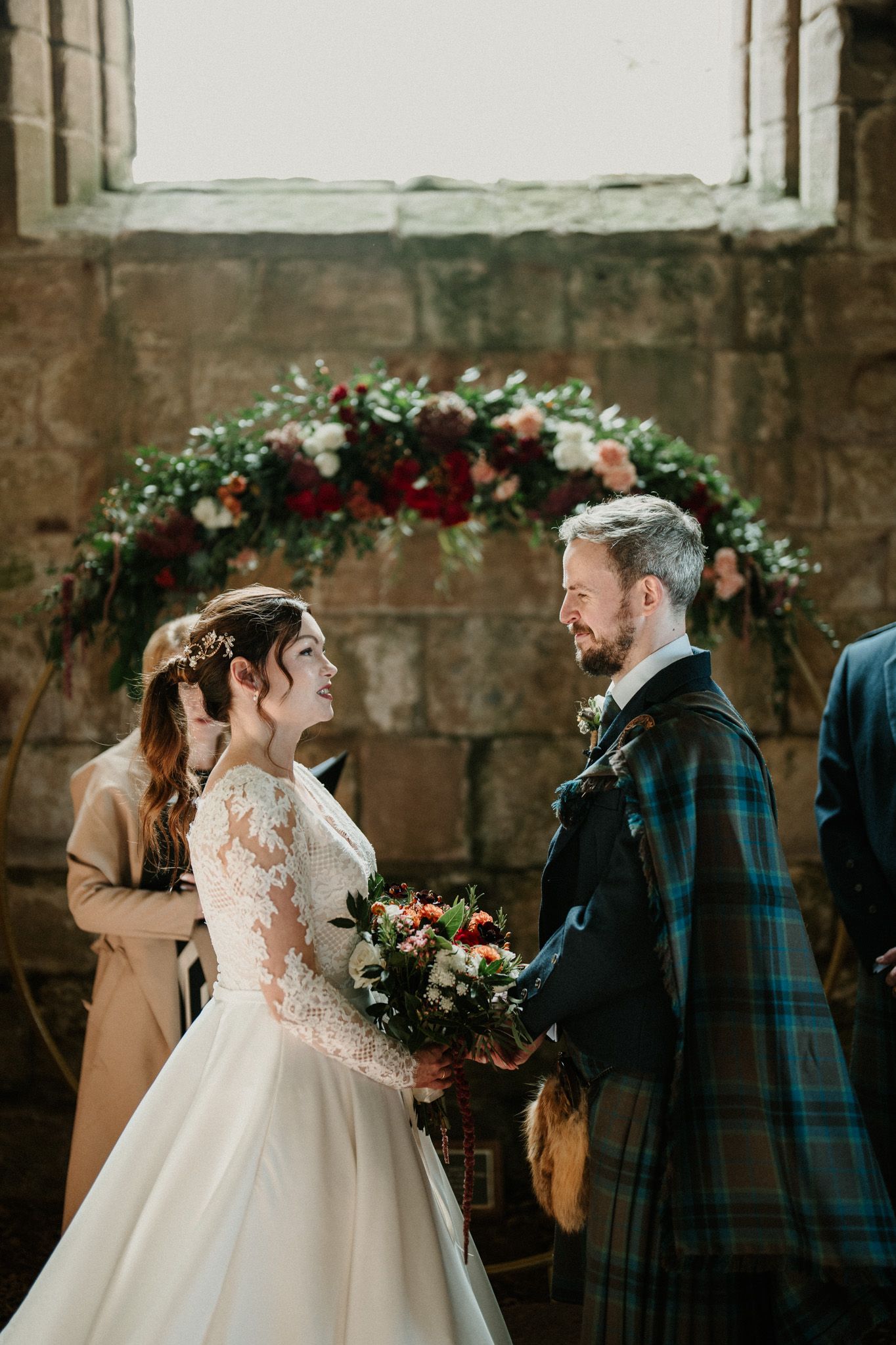 Romantic wedding ceremony moment in stone church with floral arch and natural lighting.