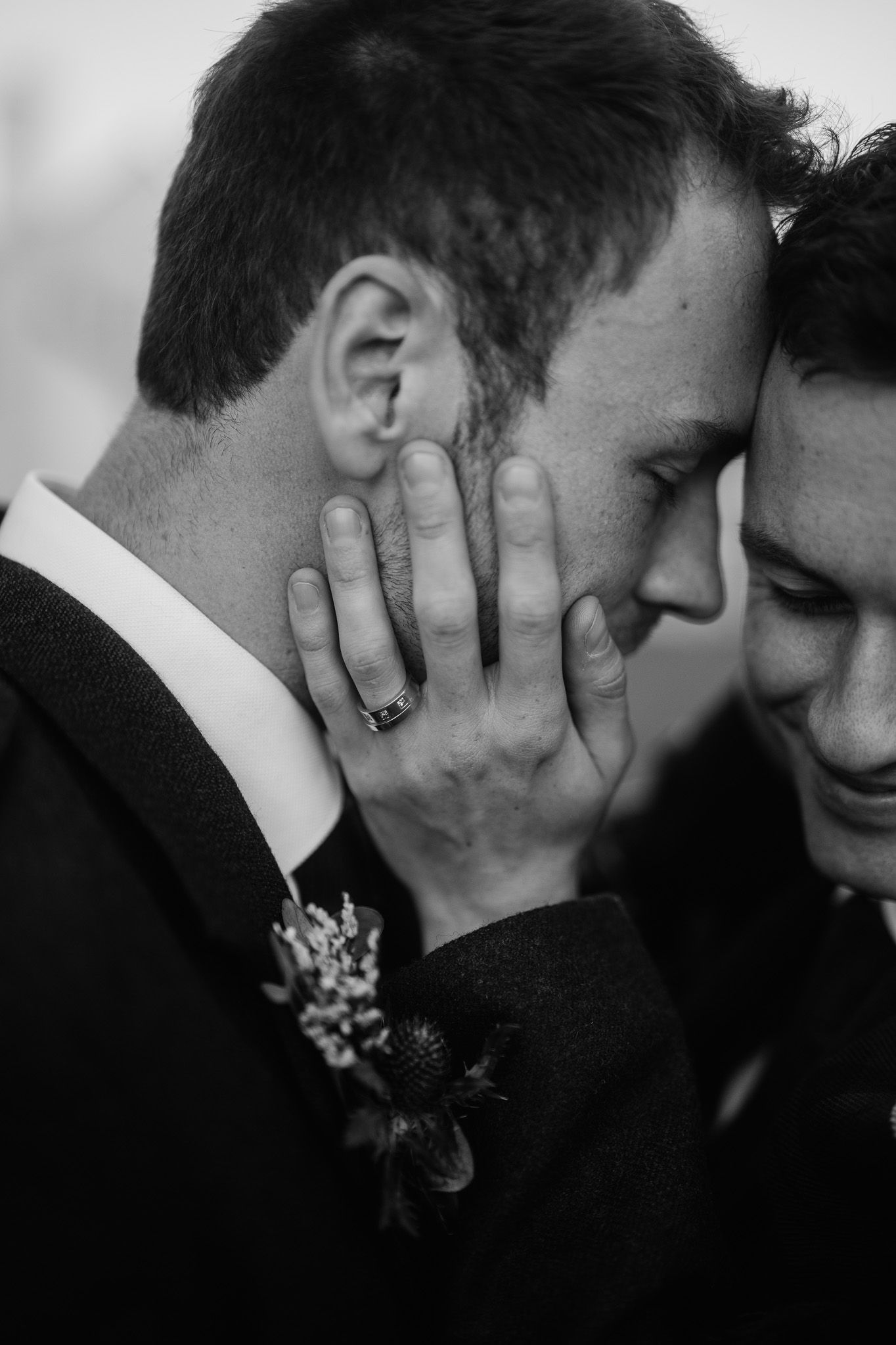 Intimate black and white portrait of two people sharing a tender moment with floral boutonniere visible.