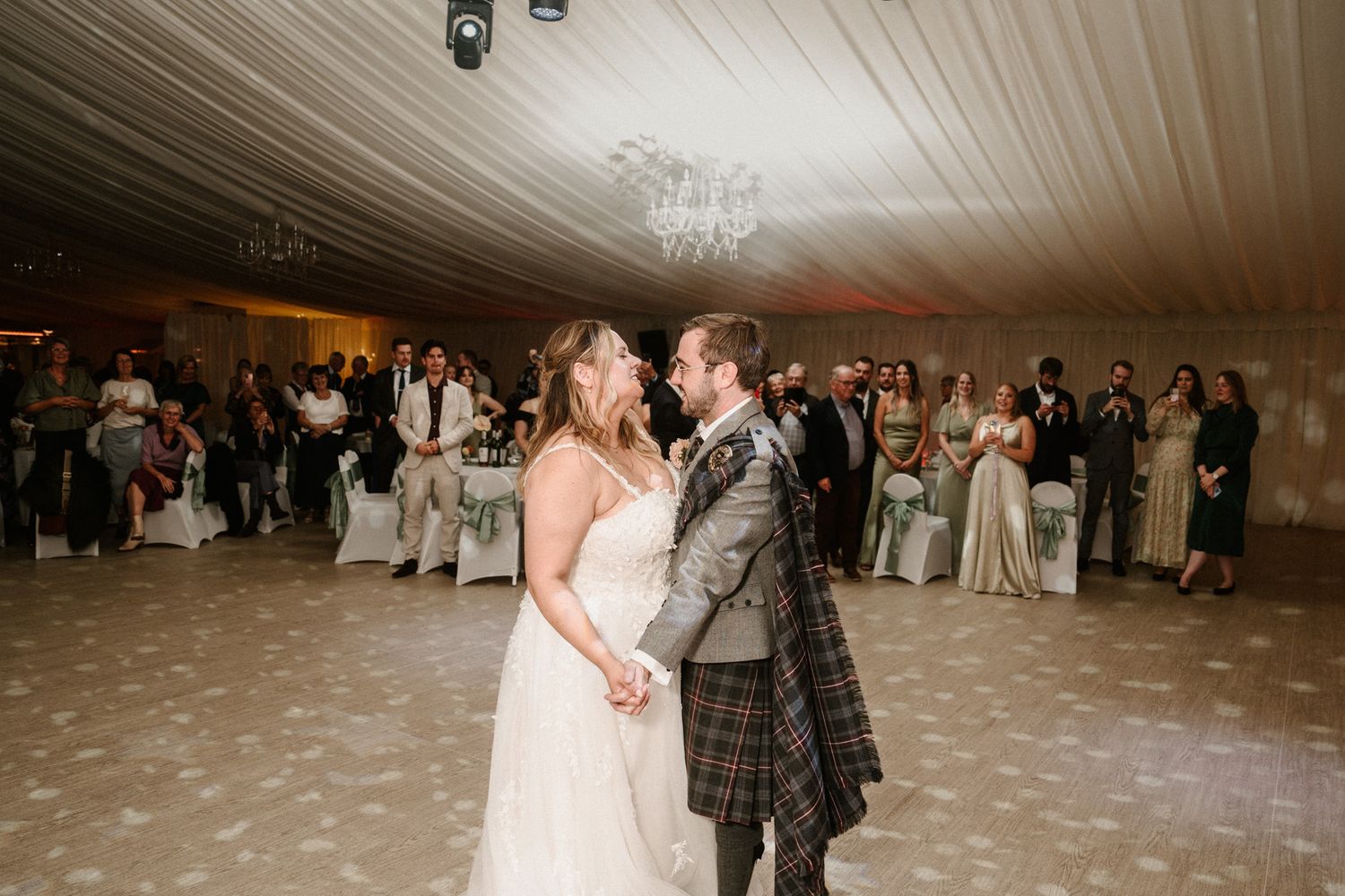 Wedding reception dance floor with white draped ceiling and chandelier lighting.