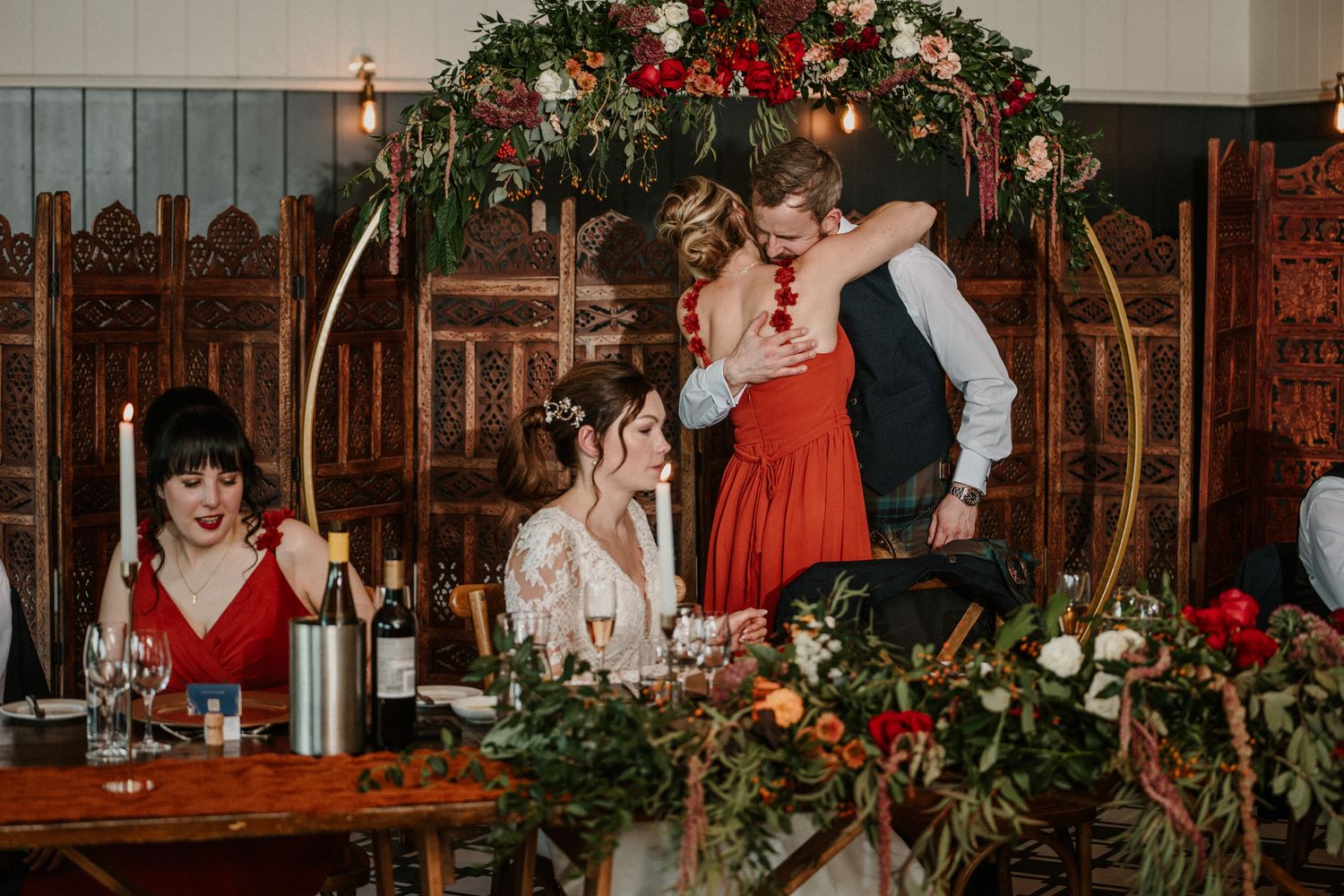 Wedding reception venue decorated with red floral arrangements and string lights.