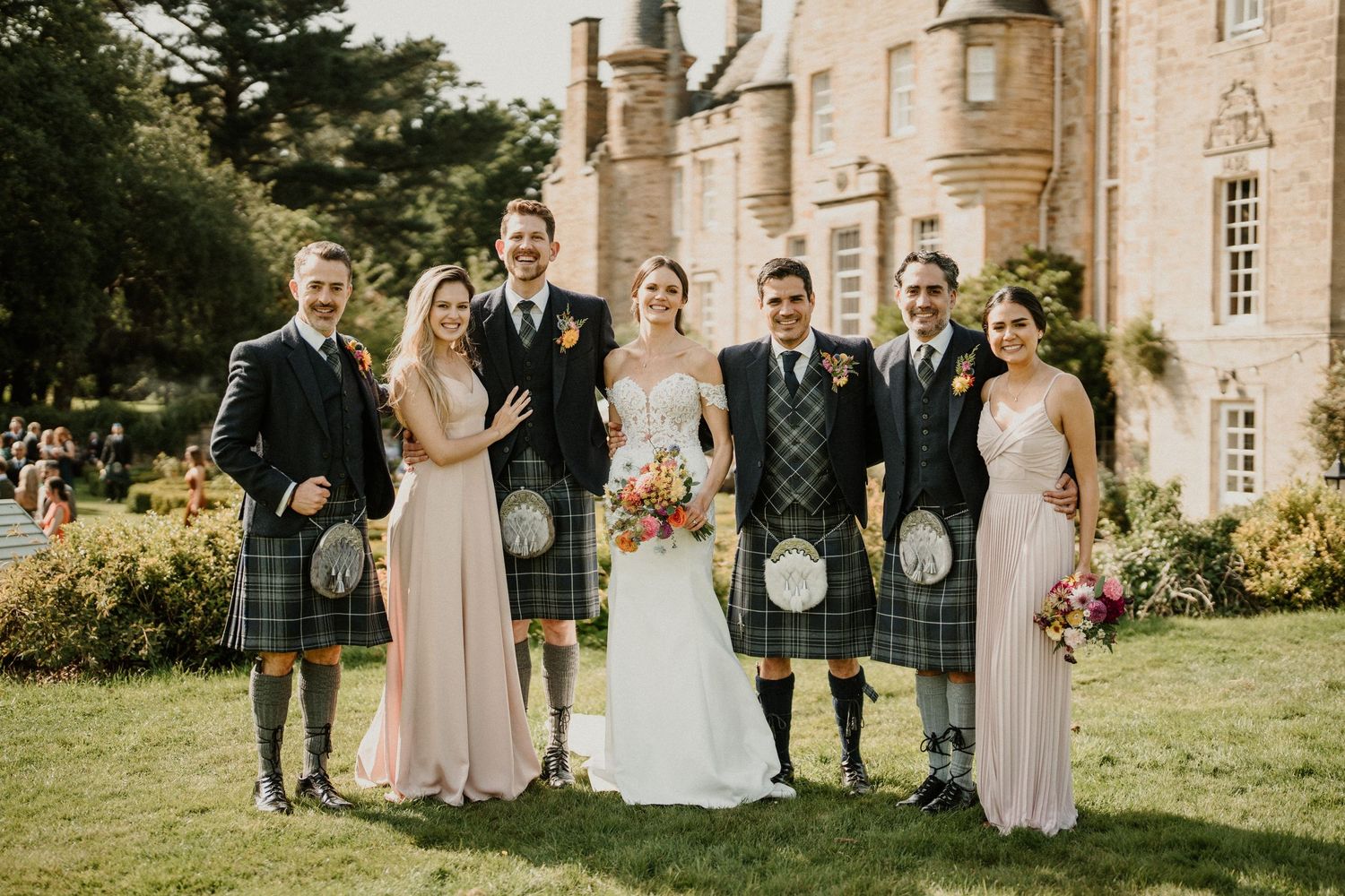 Wedding party lineup against historic castle backdrop in Scottish formal wear.