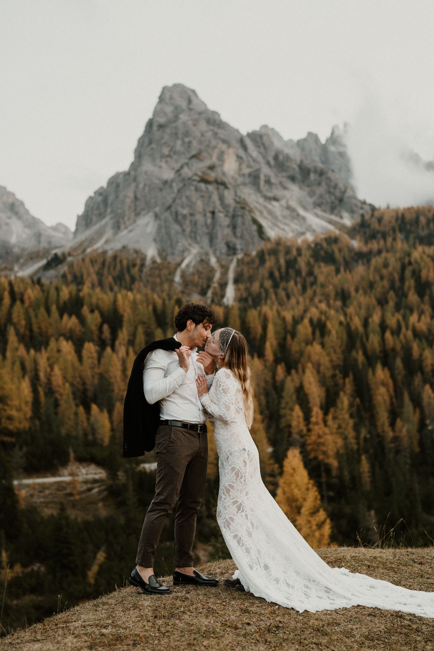 Newlyweds embrace in a scenic mountain meadow surrounded by golden autumn larches.