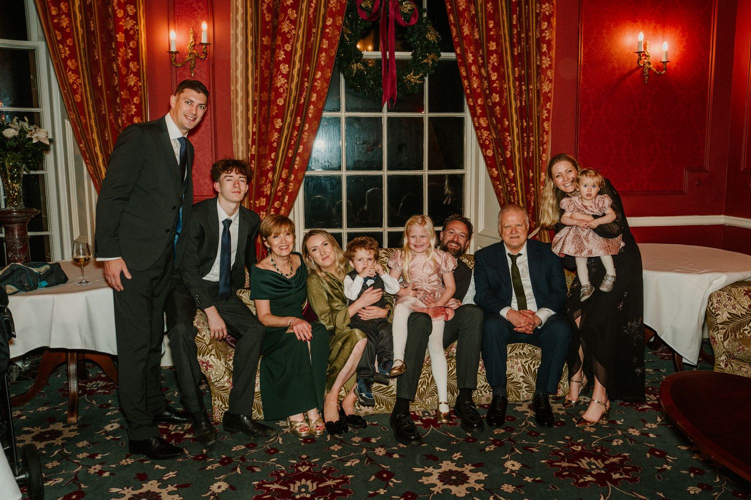 Wedding reception guests celebrate in a luxurious red-walled room with dramatic lighting.