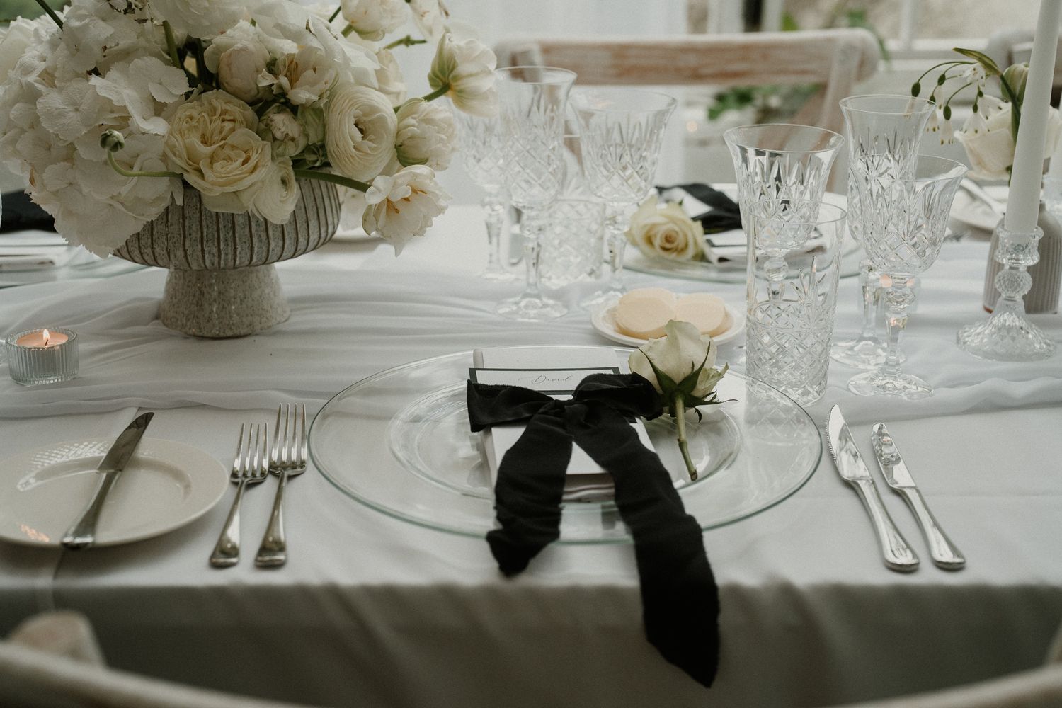 Formal place setting at wedding reception with white flowers and black ribbon detail.