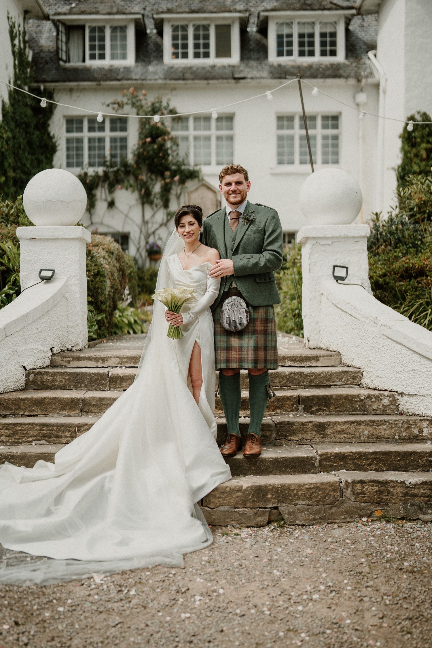 Wedding couple posing on stone steps outside a white building with traditional architecture.