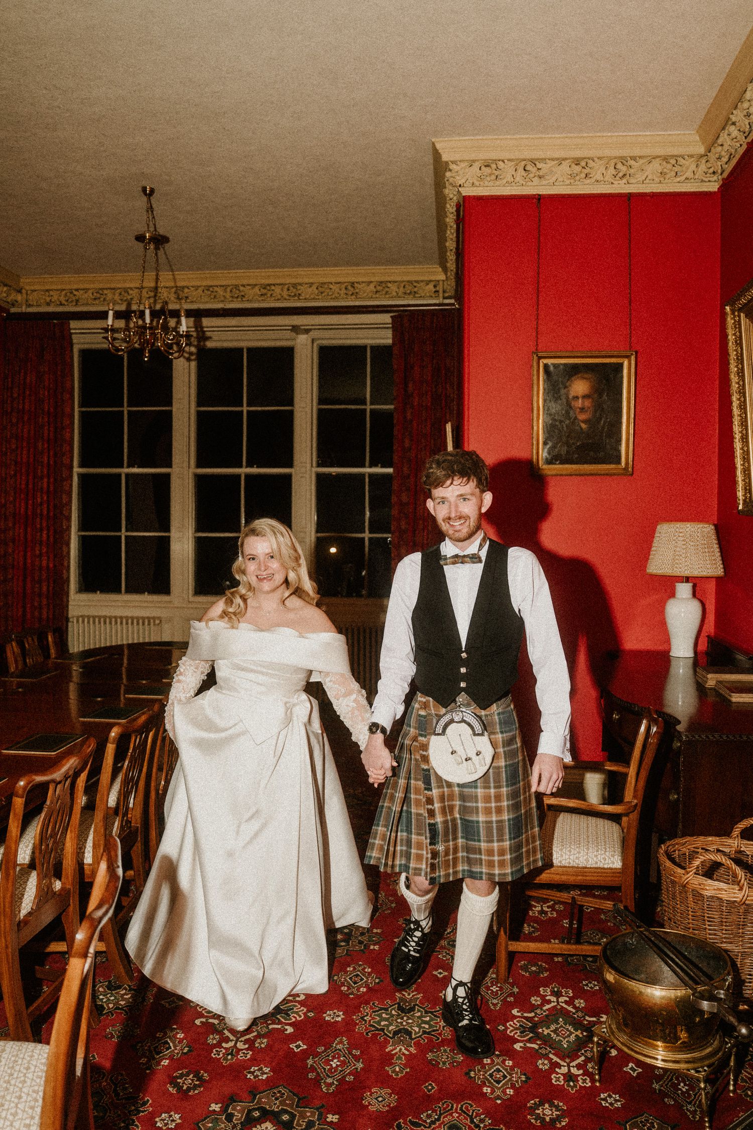 Traditional Scottish and formal attire in a classic room with red walls and vintage furniture.