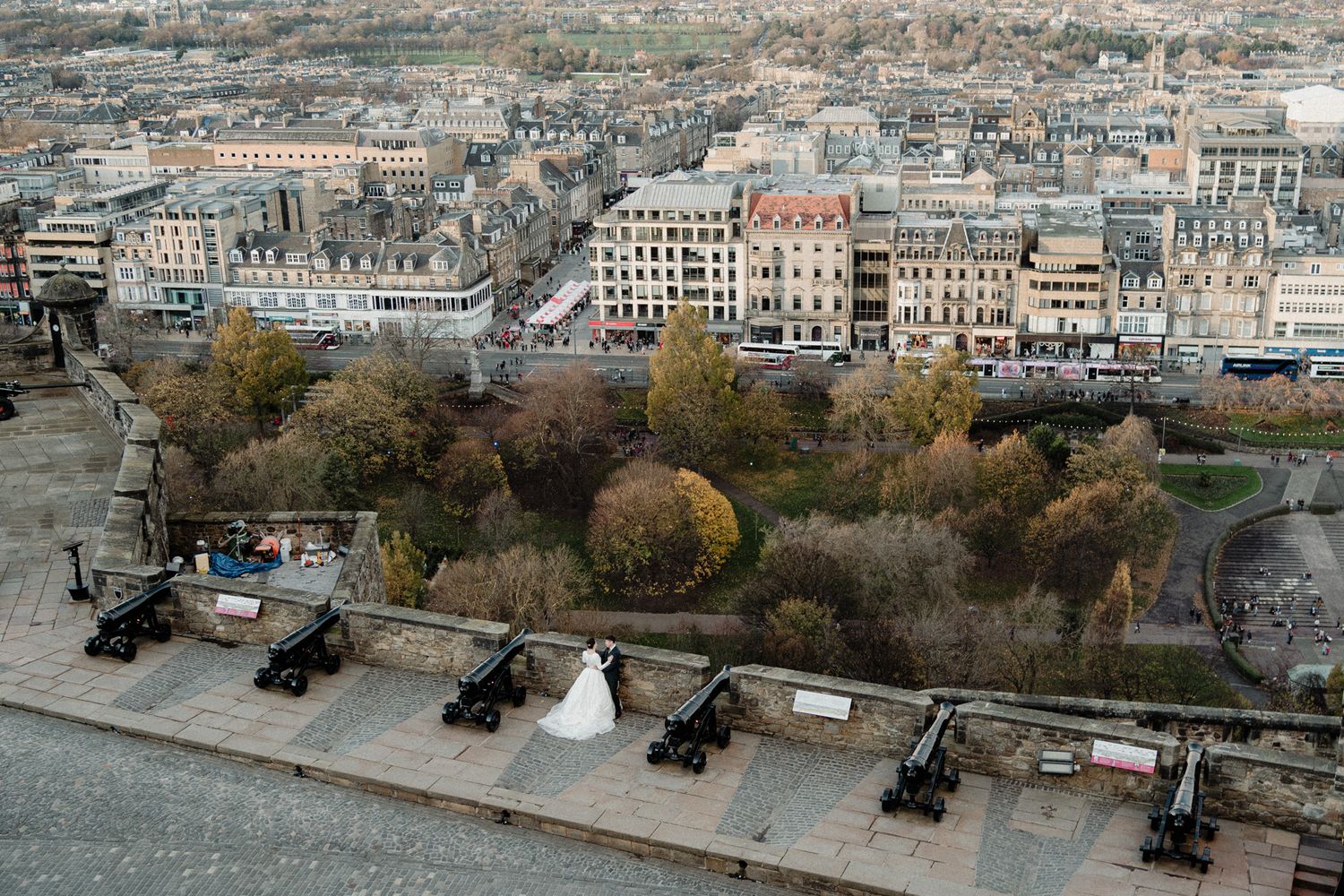 Aerial view of wedding couple among cannons with Edinburgh cityscape below.