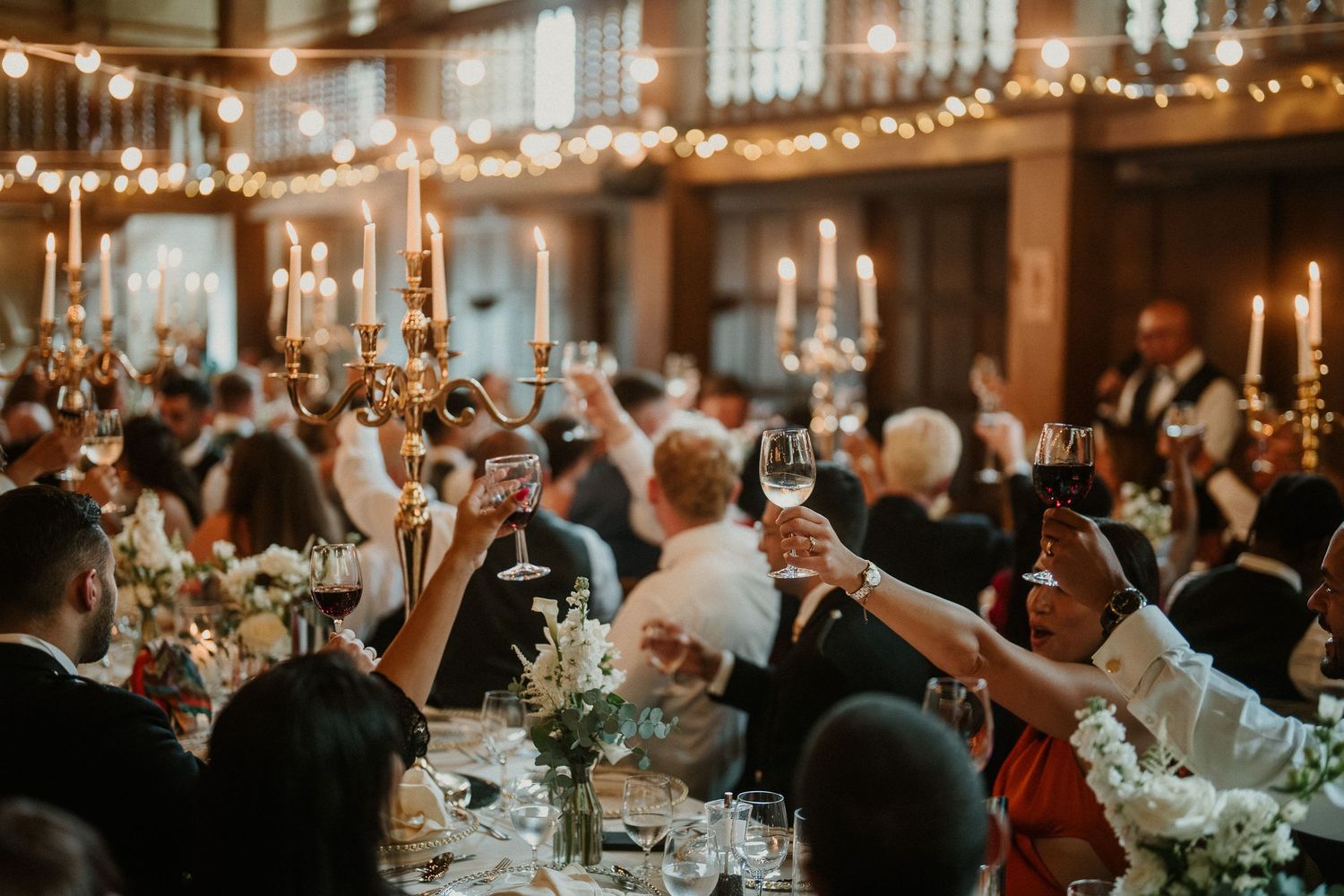 Wedding reception guests celebrating at elegantly decorated tables under ambient lighting.