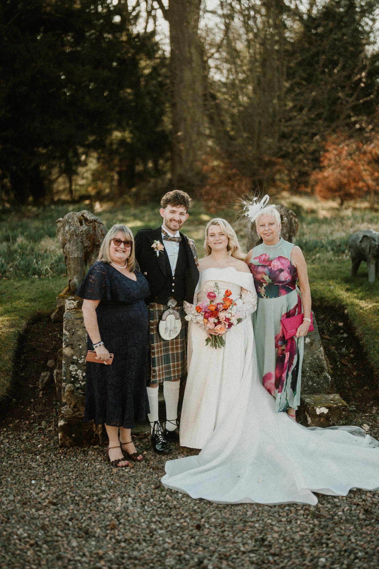 Wedding party in traditional Scottish attire poses together against a scenic outdoor backdrop.