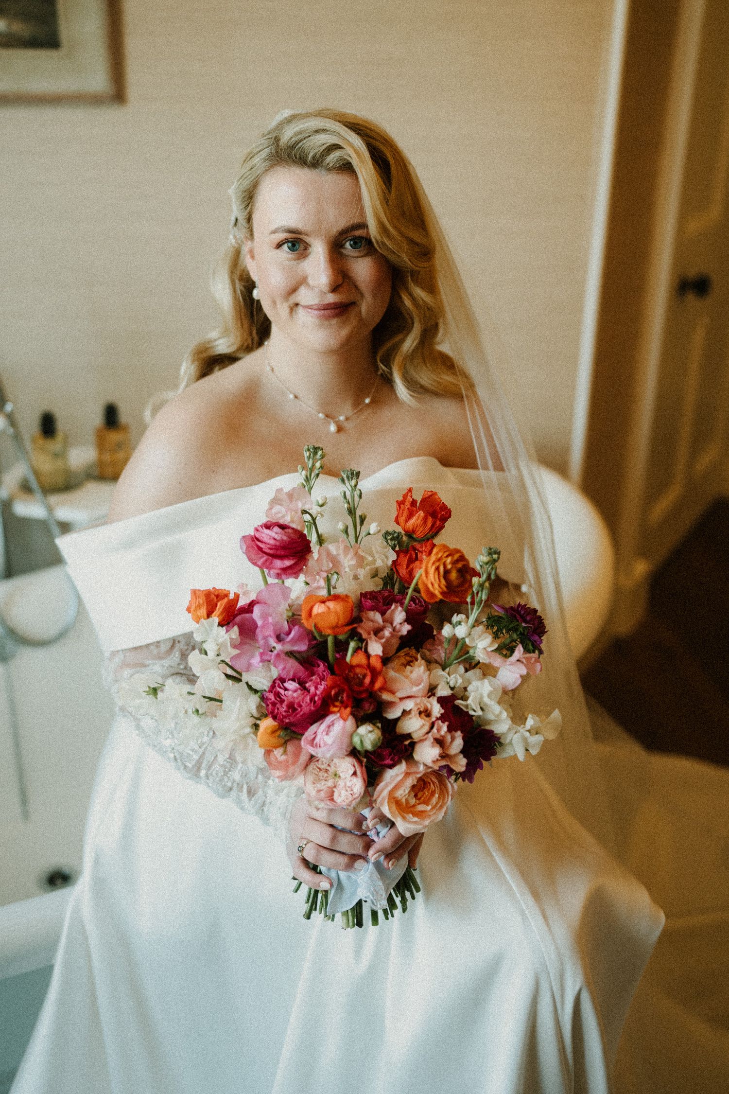 A vibrant bouquet of pink and orange flowers complements the white wedding gown.