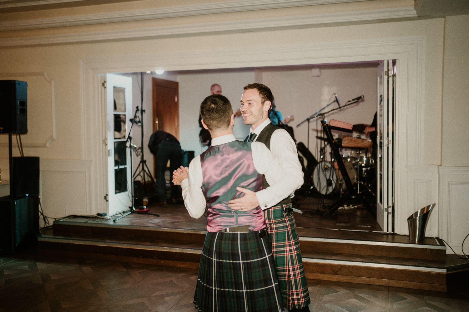 Two people in traditional Scottish kilts dance together at a wedding reception.