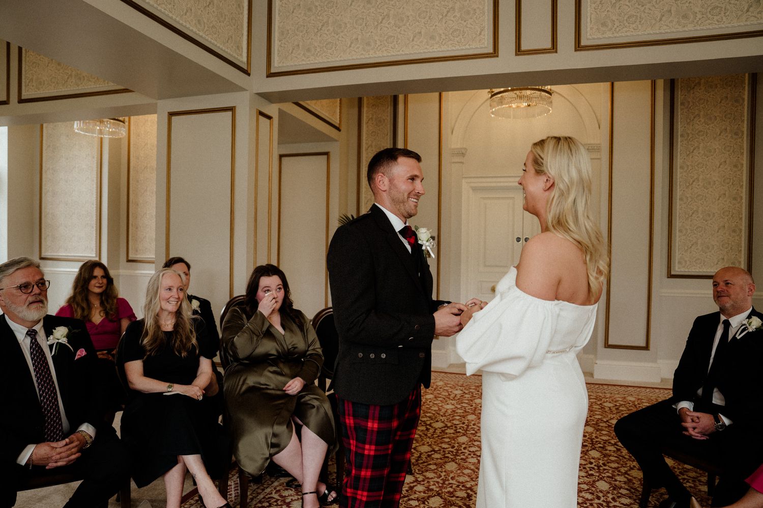 Elegant wedding reception in a bright room with cream walls and ornate molding features guests mingling.