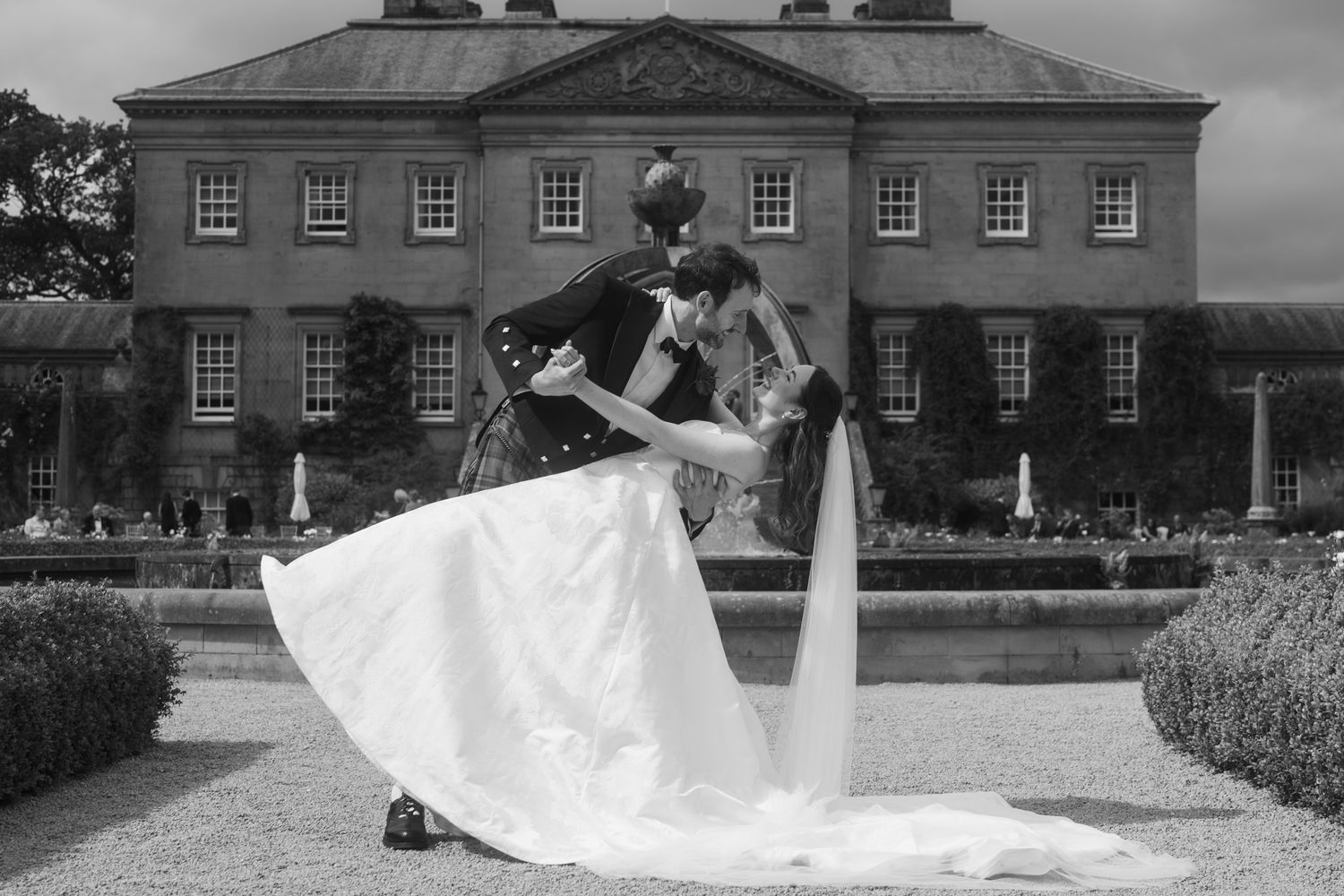 Black and white photo of bride and groom sharing a romantic dip kiss outside a grand Scottish manor house.