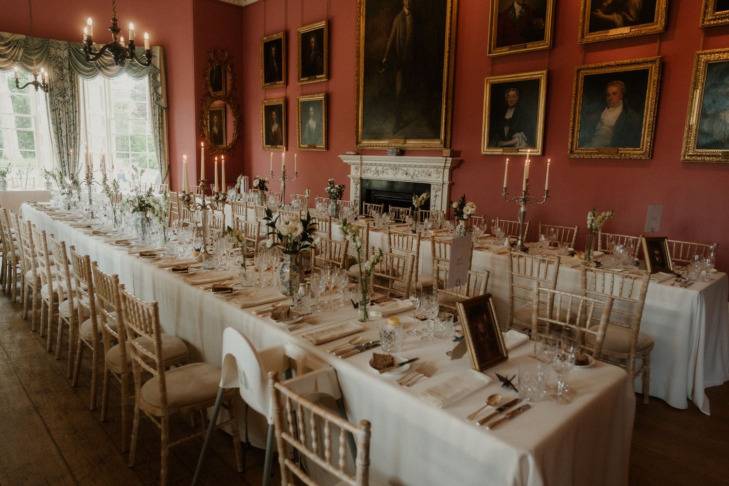 Elegant wedding reception in a grand Scottish manor with long tables, candelabras, and portrait-lined pink walls.