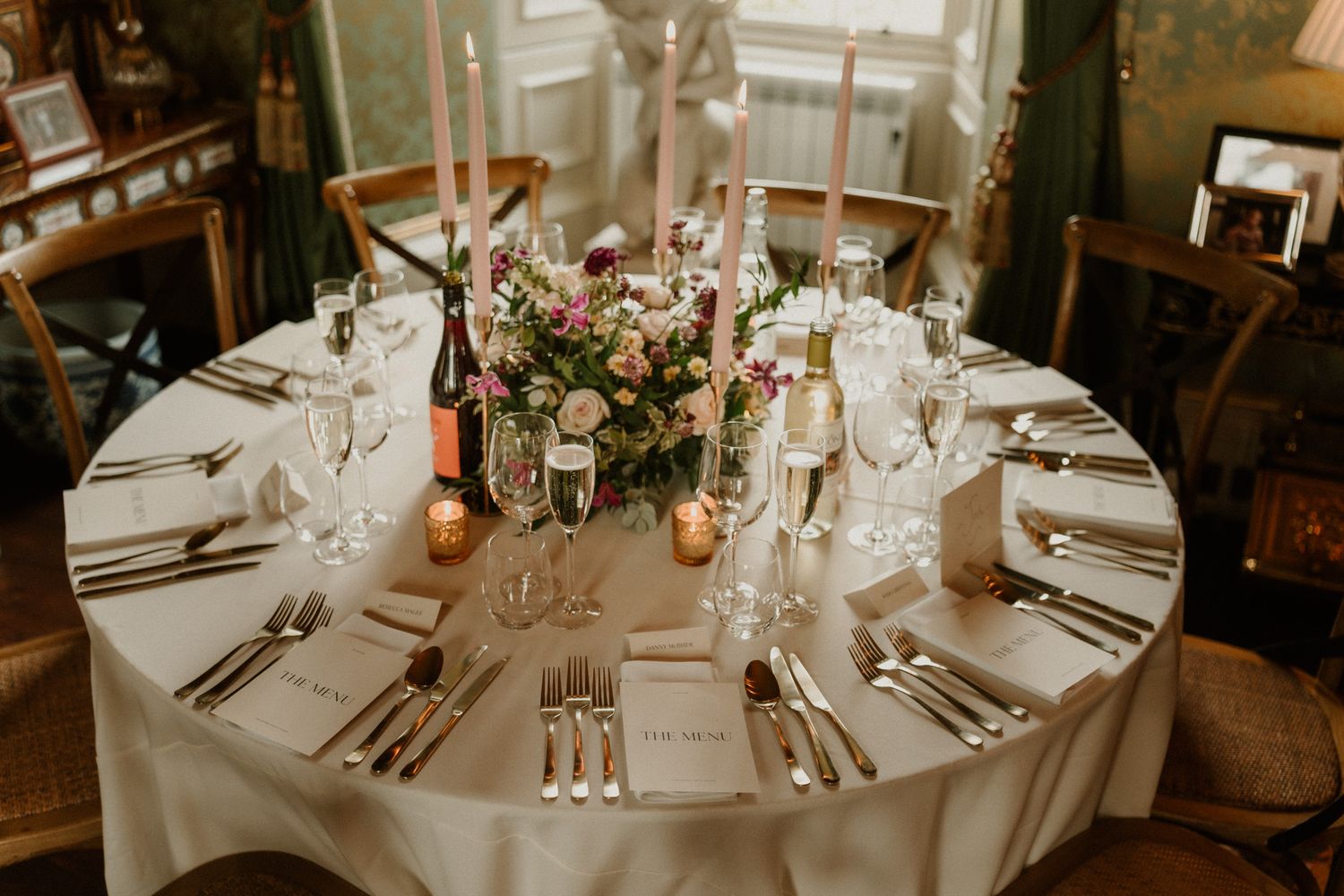 Elegant round wedding reception table with white linens, pink flowers, tall candles, crystal glasses and place settings.