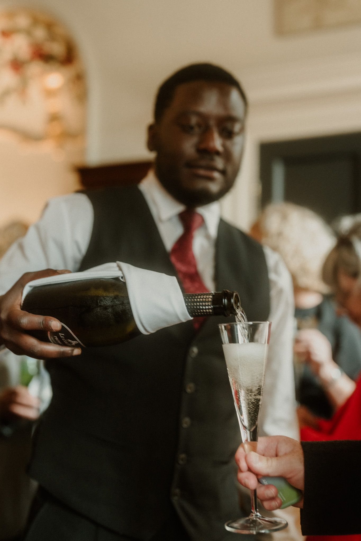 Elegant bartender in vest and red tie pouring champagne into a flute at a formal event.