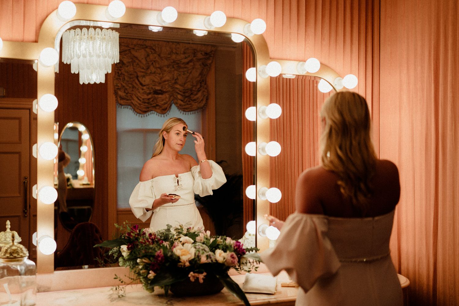 Wedding preparation scene with vanity lights and mirrors creating a warm, intimate atmosphere.